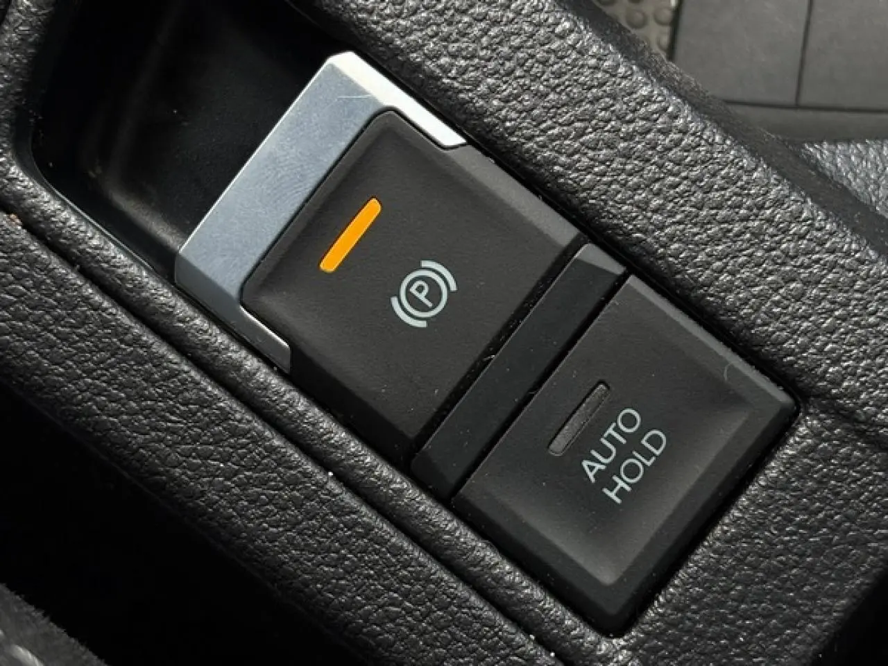 Gros plan sur le bouton de frein de stationnement électrique et fonction Auto Hold dans l’habitacle noir du Volkswagen T-Roc 2025.
