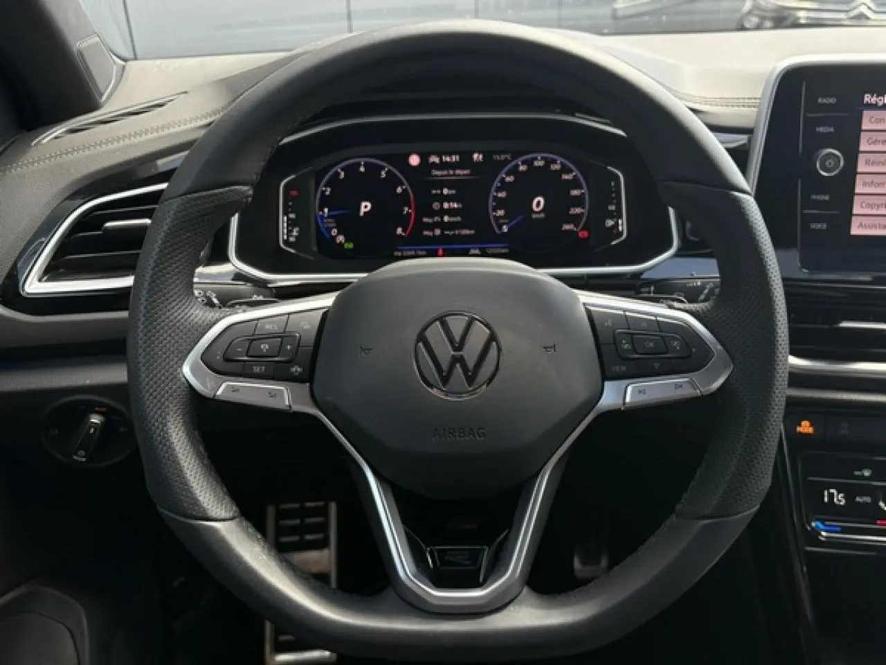 Vue rapprochée du volant cuir noir avec logo Volkswagen et tableau de bord digital du Volkswagen T-Roc 2025.