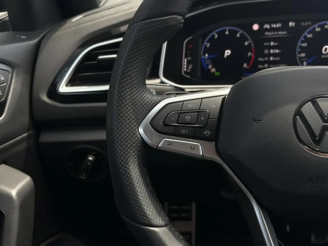Gros plan sur le volant cuir perforé noir du Volkswagen T-Roc 2025 avec commandes multifonctions et tableau de bord digital.