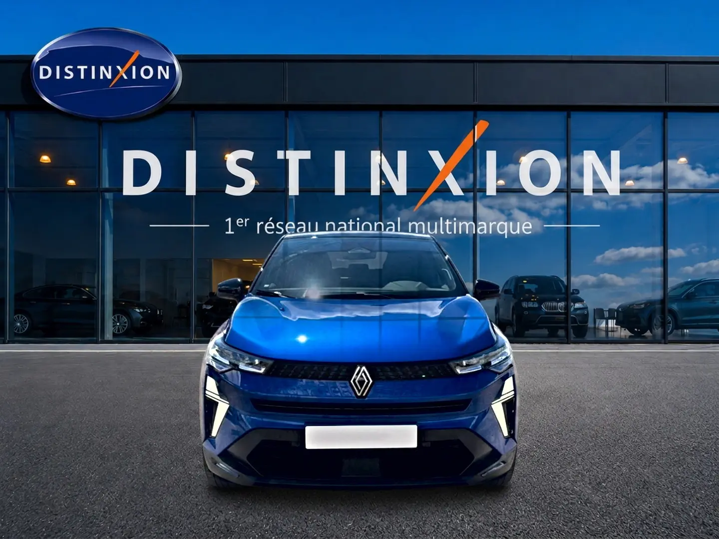 Vue avant d'un Renault Captur 2026 bleu iron avec toit noir, feux LED et calandre marquée devant un showroom Distinxion.