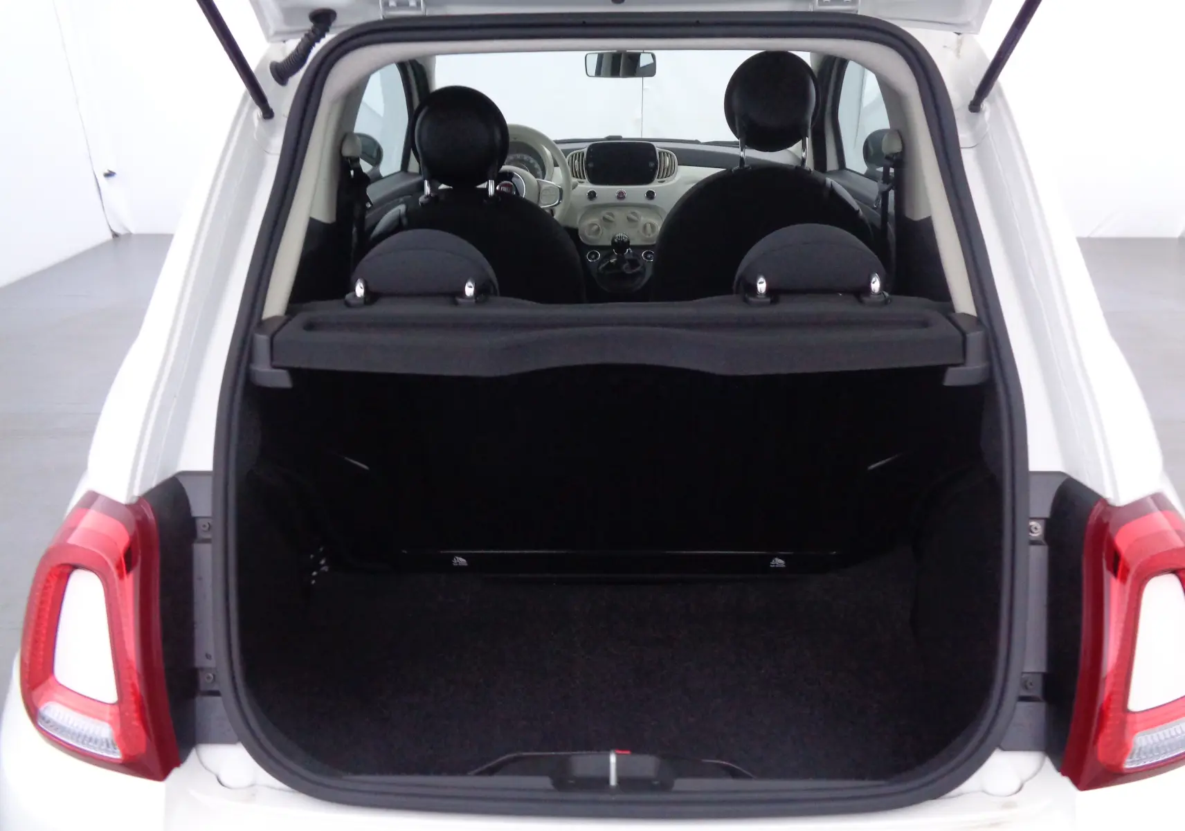 Vue arrière ouverte du coffre d'une FIAT 500 blanche Gelato, montrant l'intérieur noir et les sièges avant.