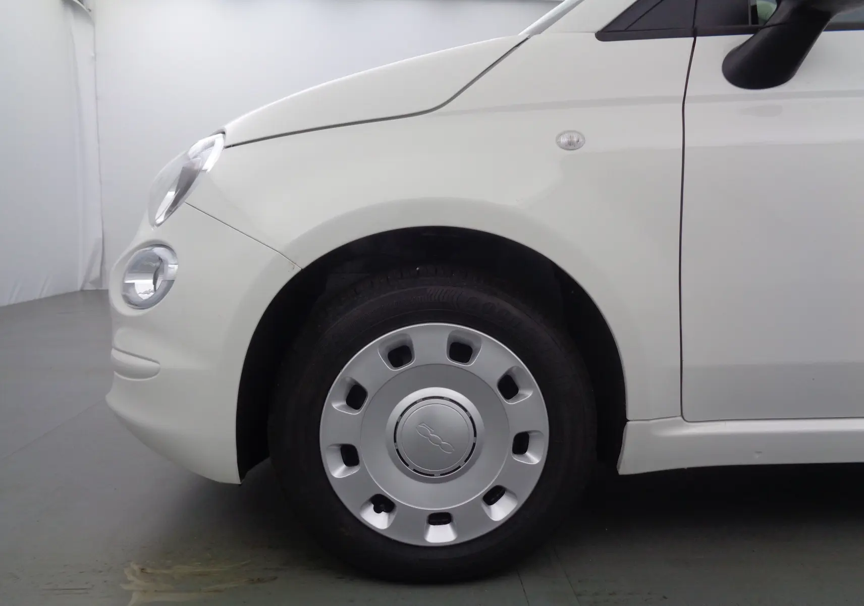 Gros plan sur la roue avant gauche d'une FIAT 500 blanche Gelato, mettant en valeur la jante et le phare rond avant.