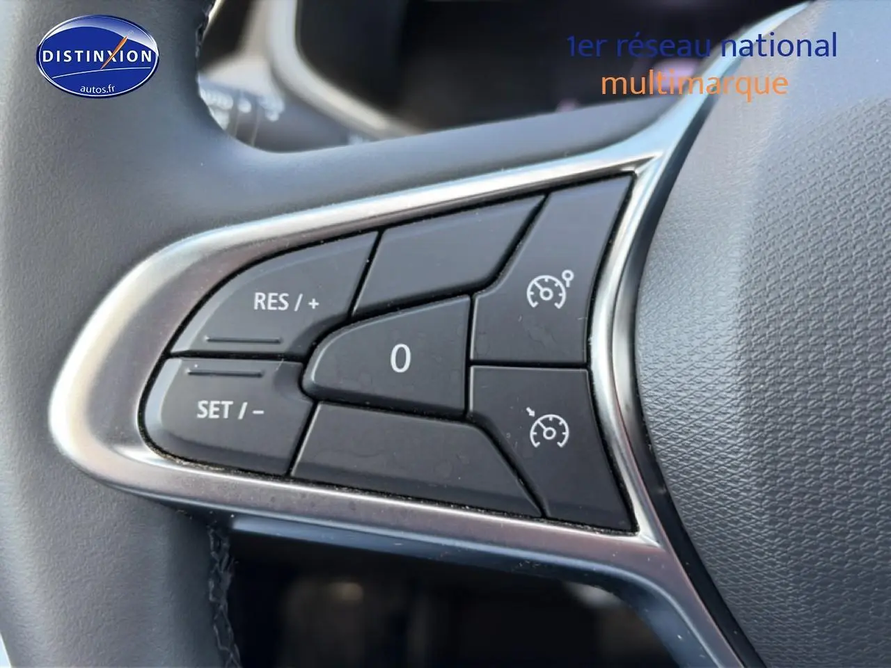 Gros plan sur les commandes noires du régulateur de vitesse au volant gris de la Renault Clio V.