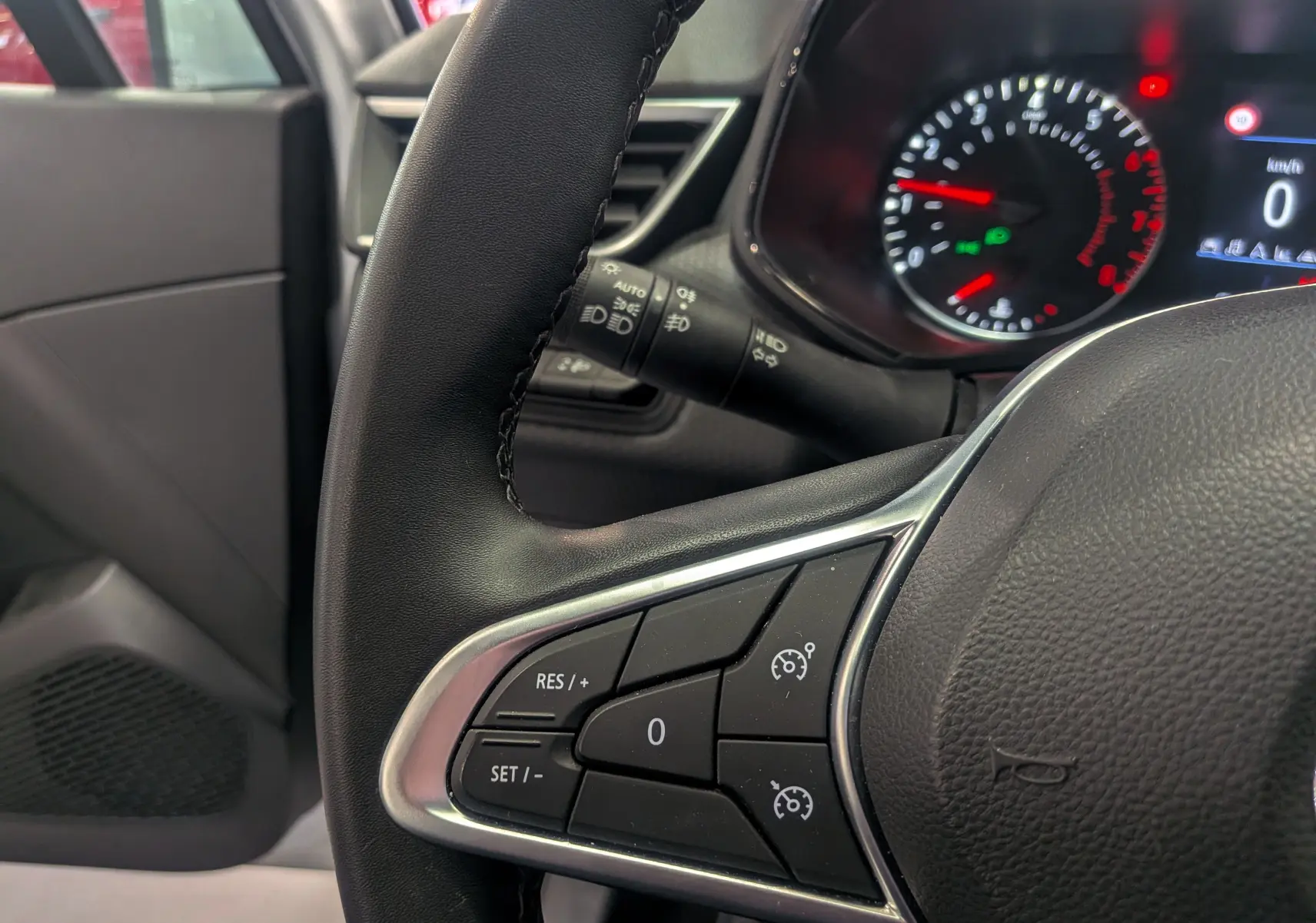 Gros plan sur le volant noir de la Renault Clio V TCe 90, avec commandes de régulateur et tableau de bord allumé.