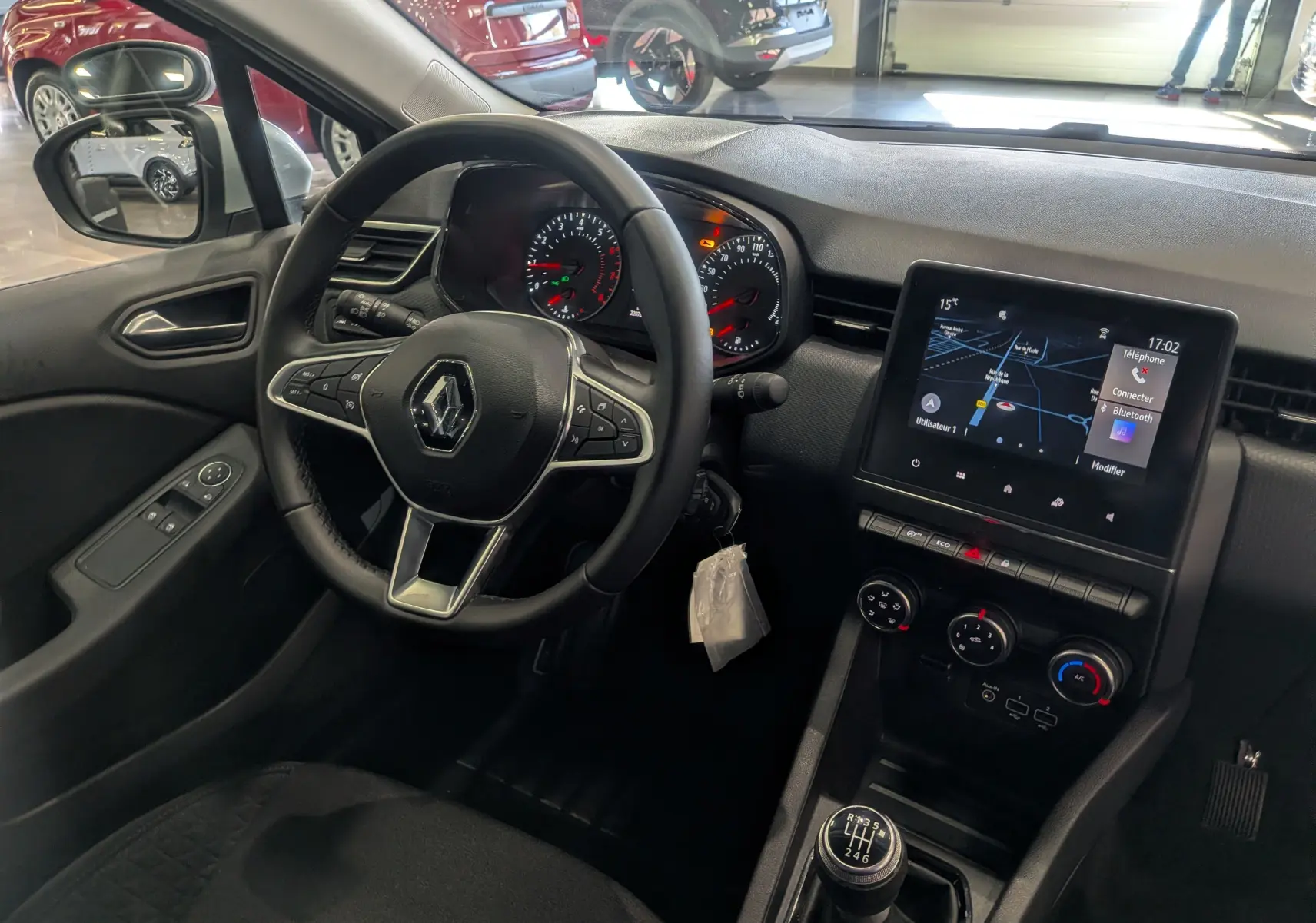 Vue intérieure côté conducteur de la Renault Clio V gris platine, avec tableau de bord digital et levier de vitesse manuel.