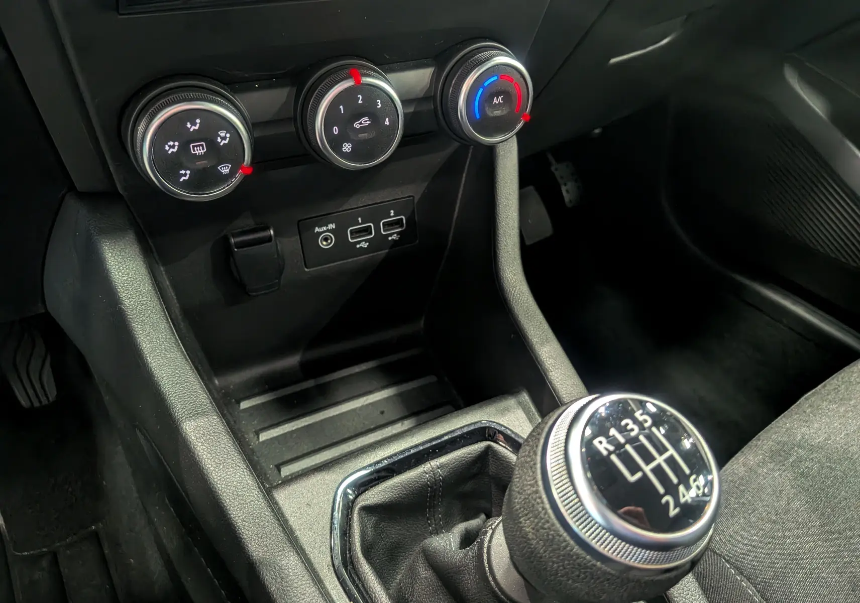 Gros plan sur la console centrale de la Renault Clio V gris platine, mettant en valeur le levier de vitesse manuel et les commandes de climatisation.