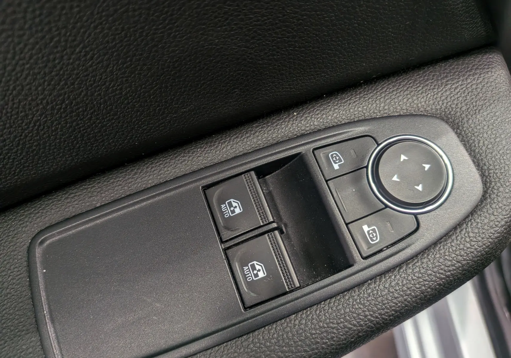 Gros plan sur les commandes de lève-vitres et réglage des rétroviseurs côté conducteur d'une Renault Clio V gris platine.