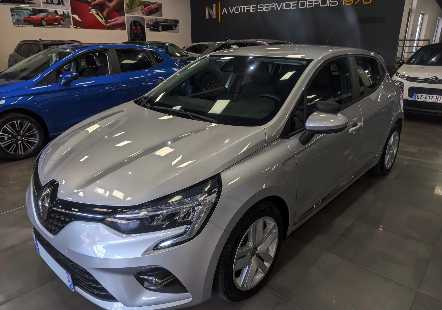 Renault Clio V gris platine vue 3/4 avant droit en showroom, avec phares LED et jantes alliage visibles.