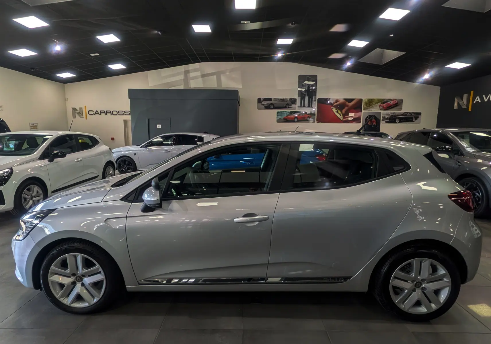 Profil côté gauche d'une Renault Clio V gris platine 2021 en showroom, avec jantes alliage et vitres teintées.