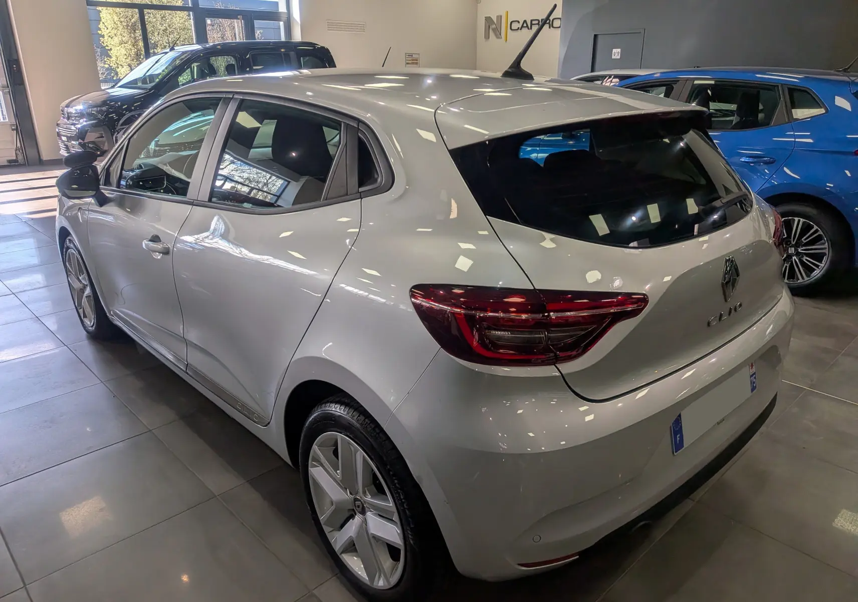 Vue 3/4 arrière droite d'une Renault Clio V gris platine en intérieur, avec feux arrière LED et jantes alliage.