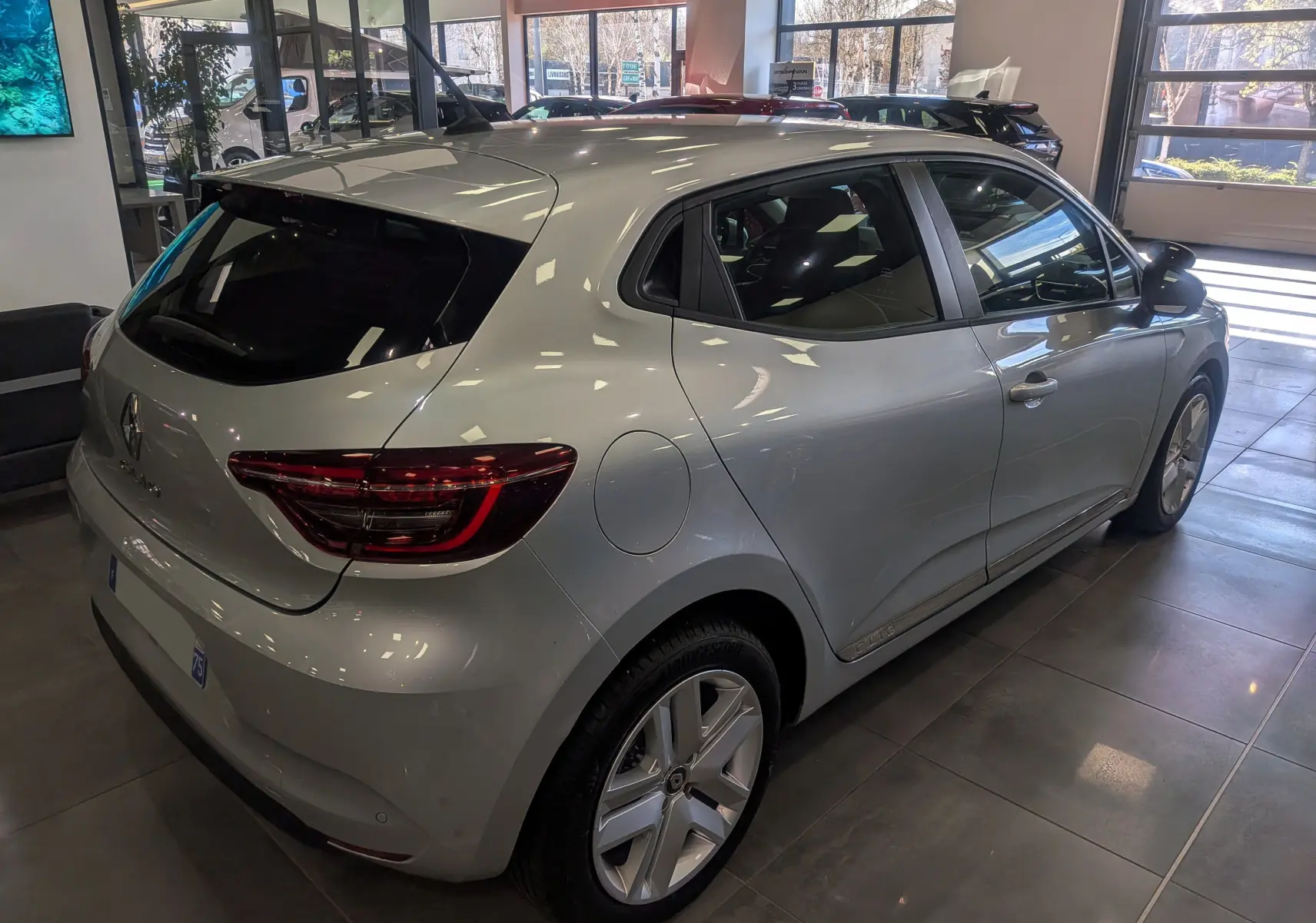Vue 3/4 arrière droite d'une Renault Clio V gris platine en showroom, avec feux arrière LED et jantes alliage.