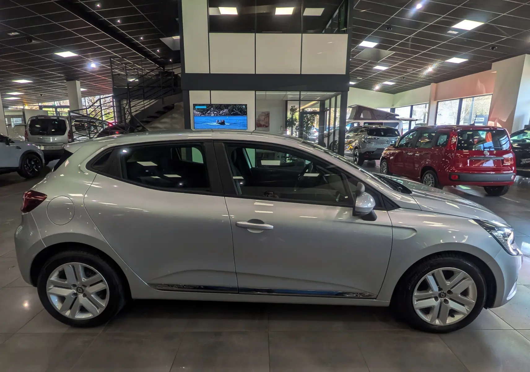 Profil côté droit d'une Renault Clio V gris platine 2021 en intérieur, avec jantes alliage et poignées de porte intégrées.