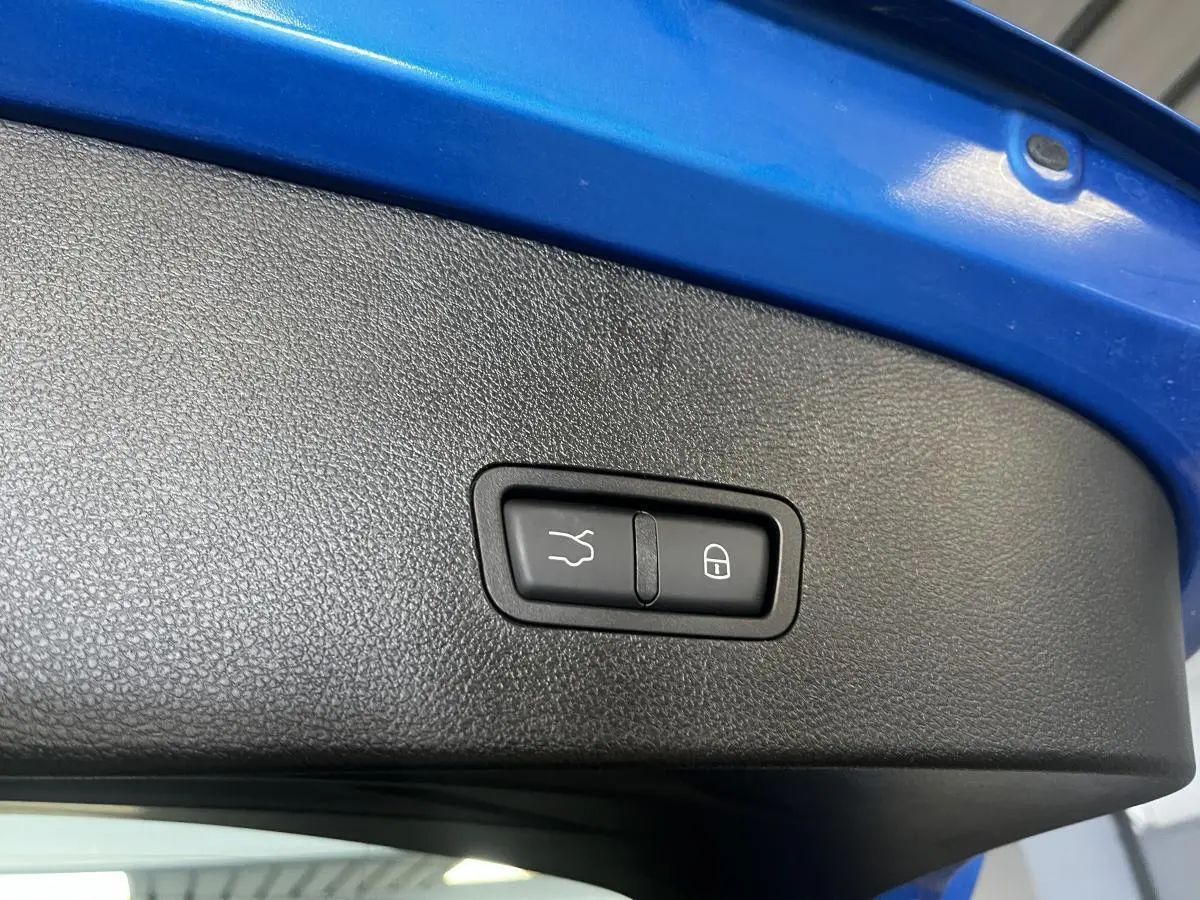 Gros plan sur le bouton d'ouverture et de verrouillage du hayon électrique, intérieur du coffre bleu visible.