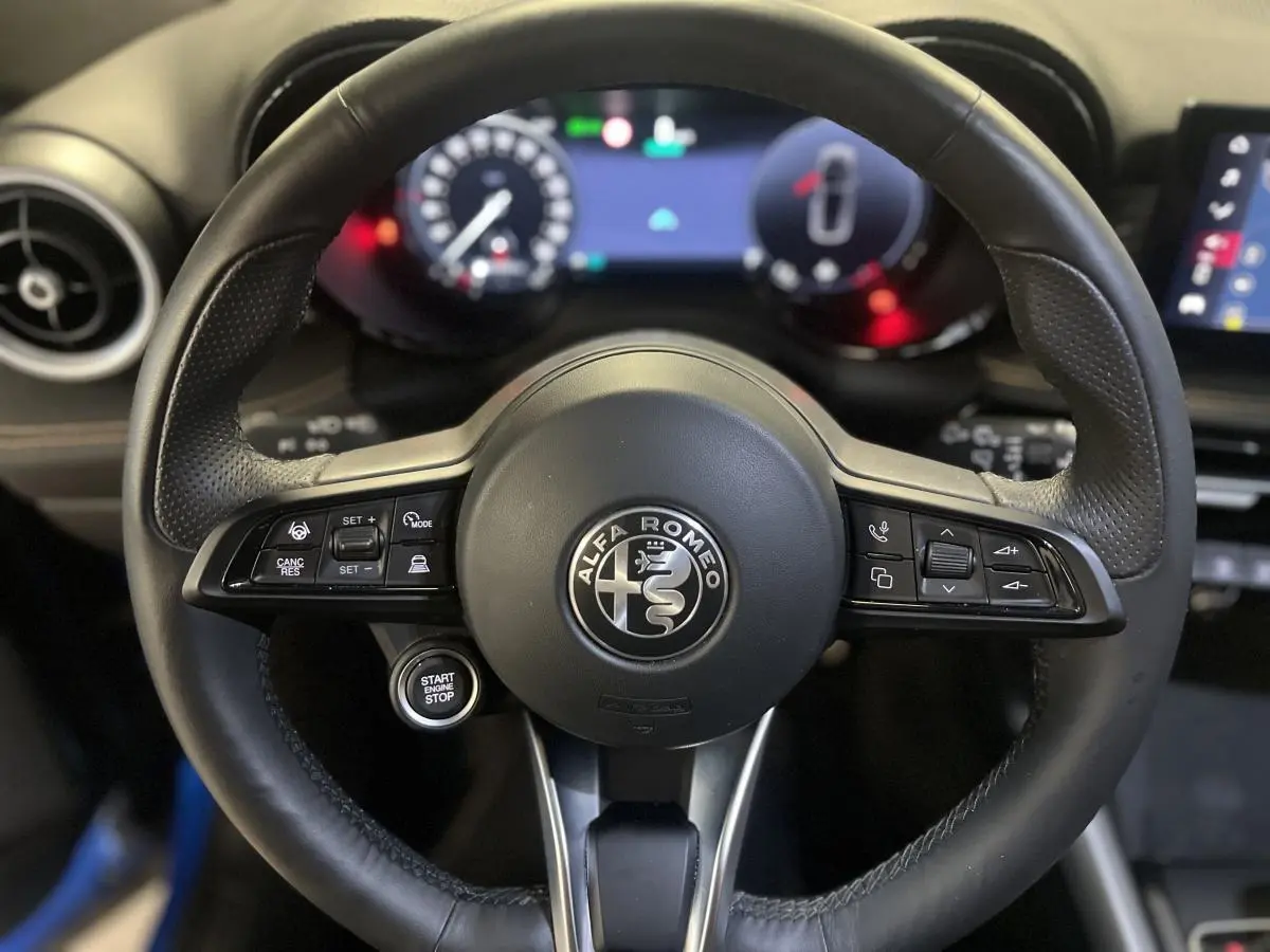 Gros plan sur le volant cuir noir d'Alfa Romeo Tonale 2024 avec commandes intégrées et logo central visible.