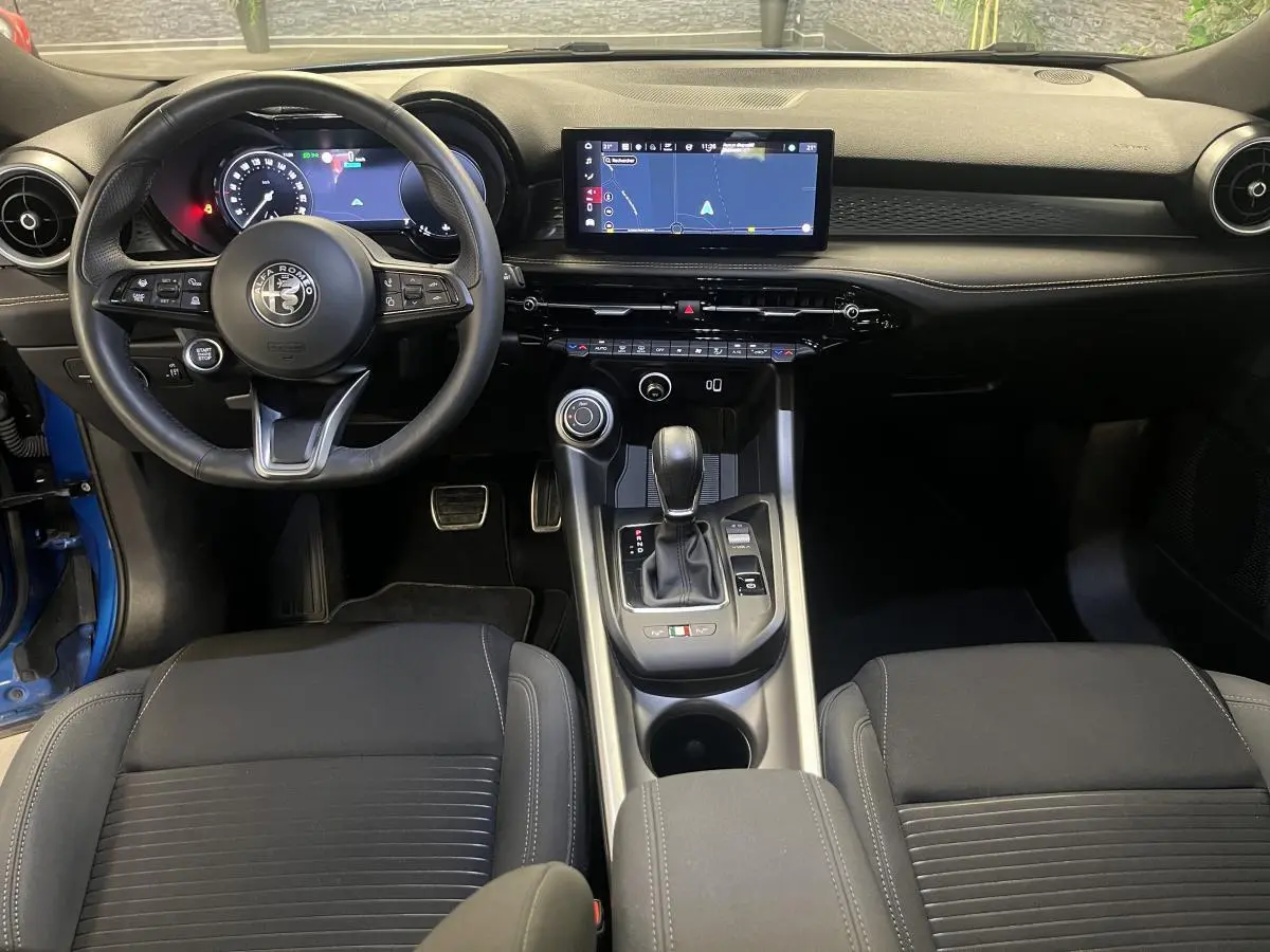 Vue intérieure avant de l'Alfa Romeo Tonale 2024, tableau de bord noir avec écran tactile et volant sport en cuir.