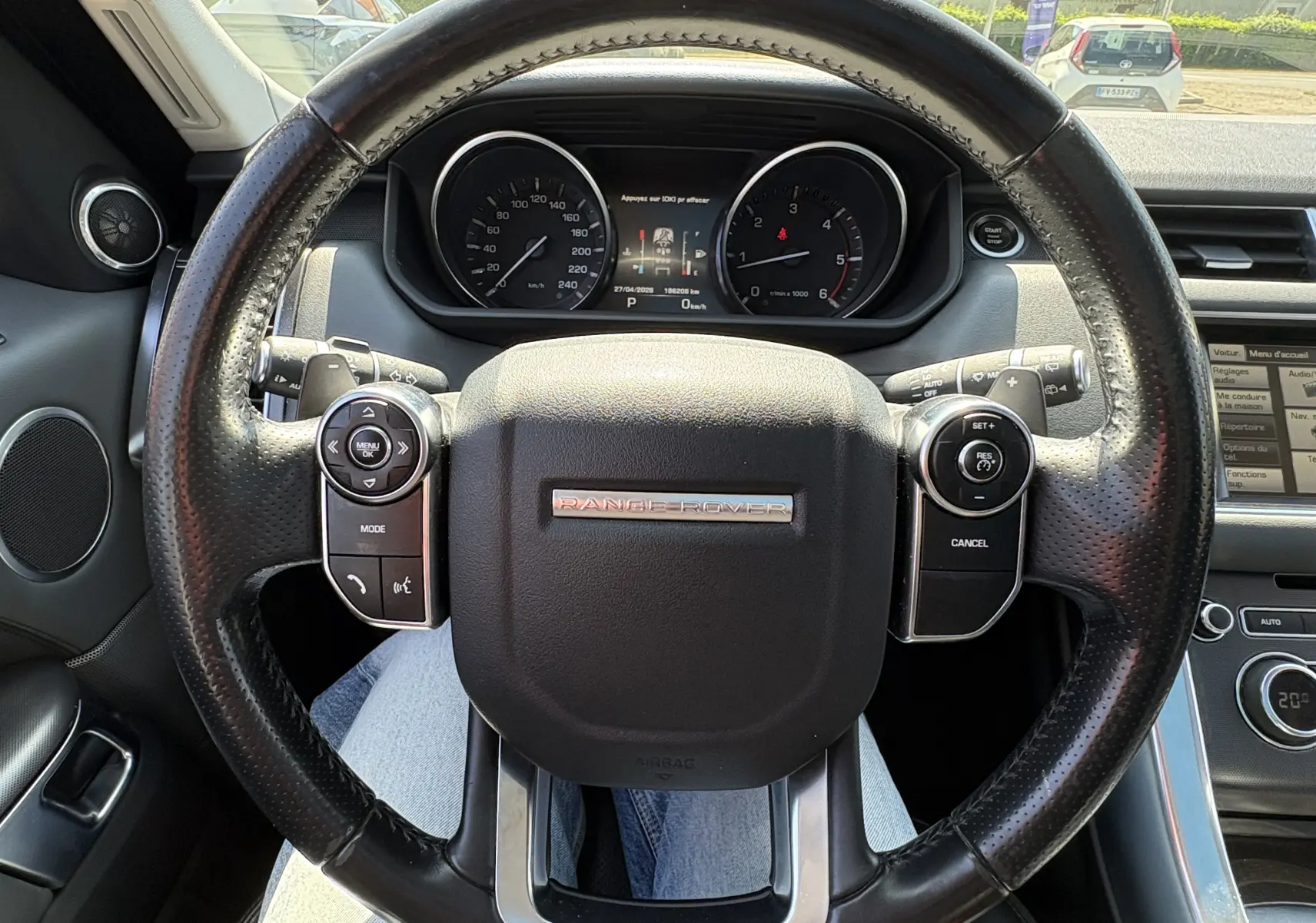 Vue rapprochée du volant noir perforé du Range Rover Sport 2015, avec tableau de bord et commandes visibles en arrière-plan.