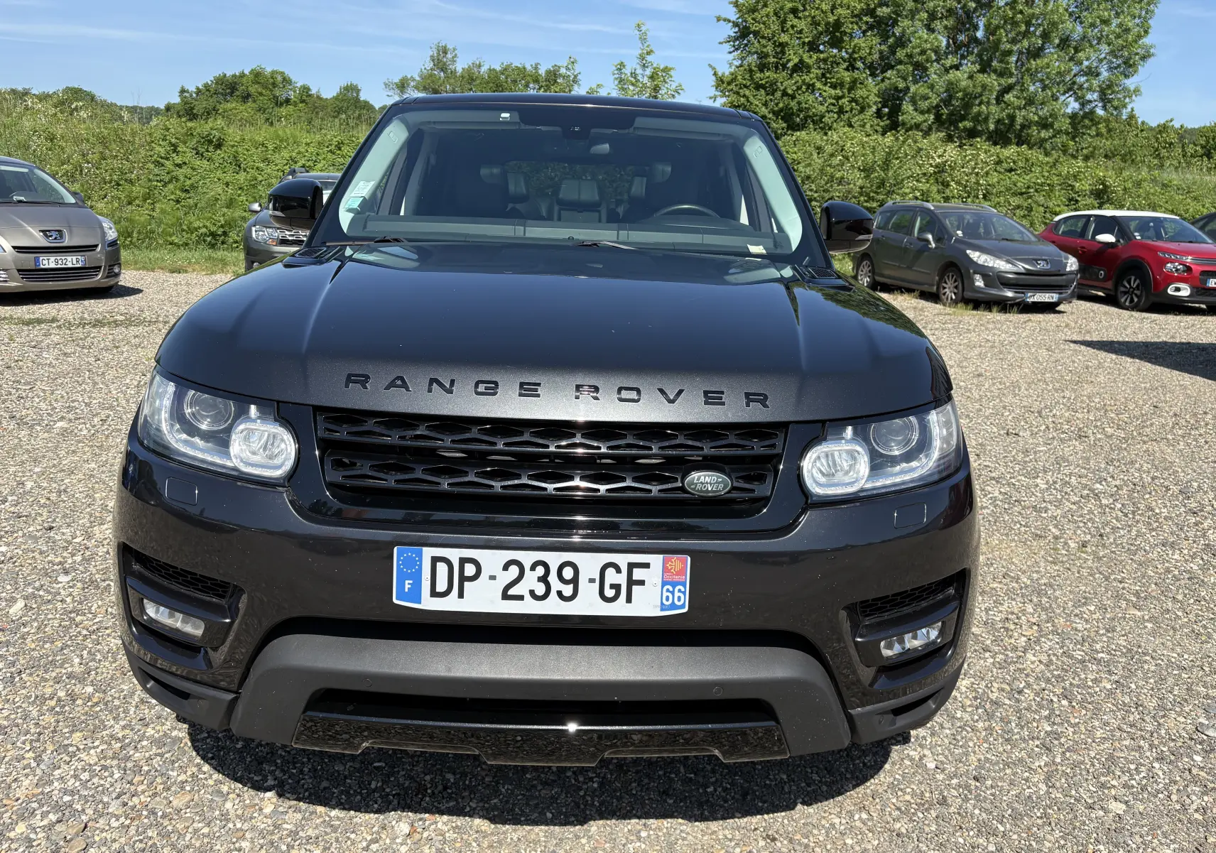 Vue avant d'un Range Rover Sport Mark III noir brillant, avec calandre et phares LED distinctifs, sur un parking extérieur.