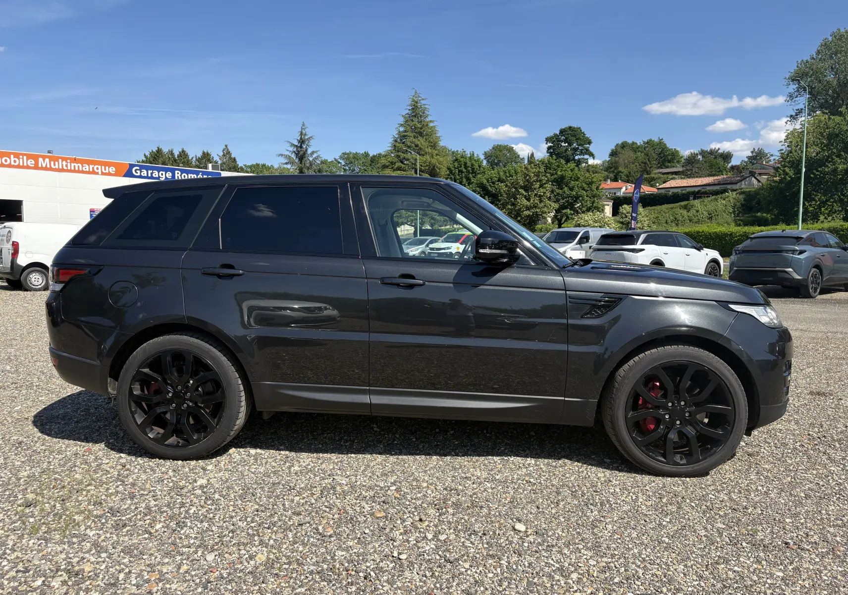 Vue de profil côté gauche d'un Range Rover Sport 2015 noir avec jantes noires et étriers rouges sur un parking.