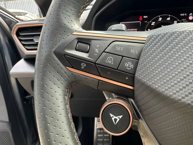 Gros plan sur le volant cuir perforé côté gauche du CUPRA Formentor gris, avec commandes multifonctions et logo central cuivré.