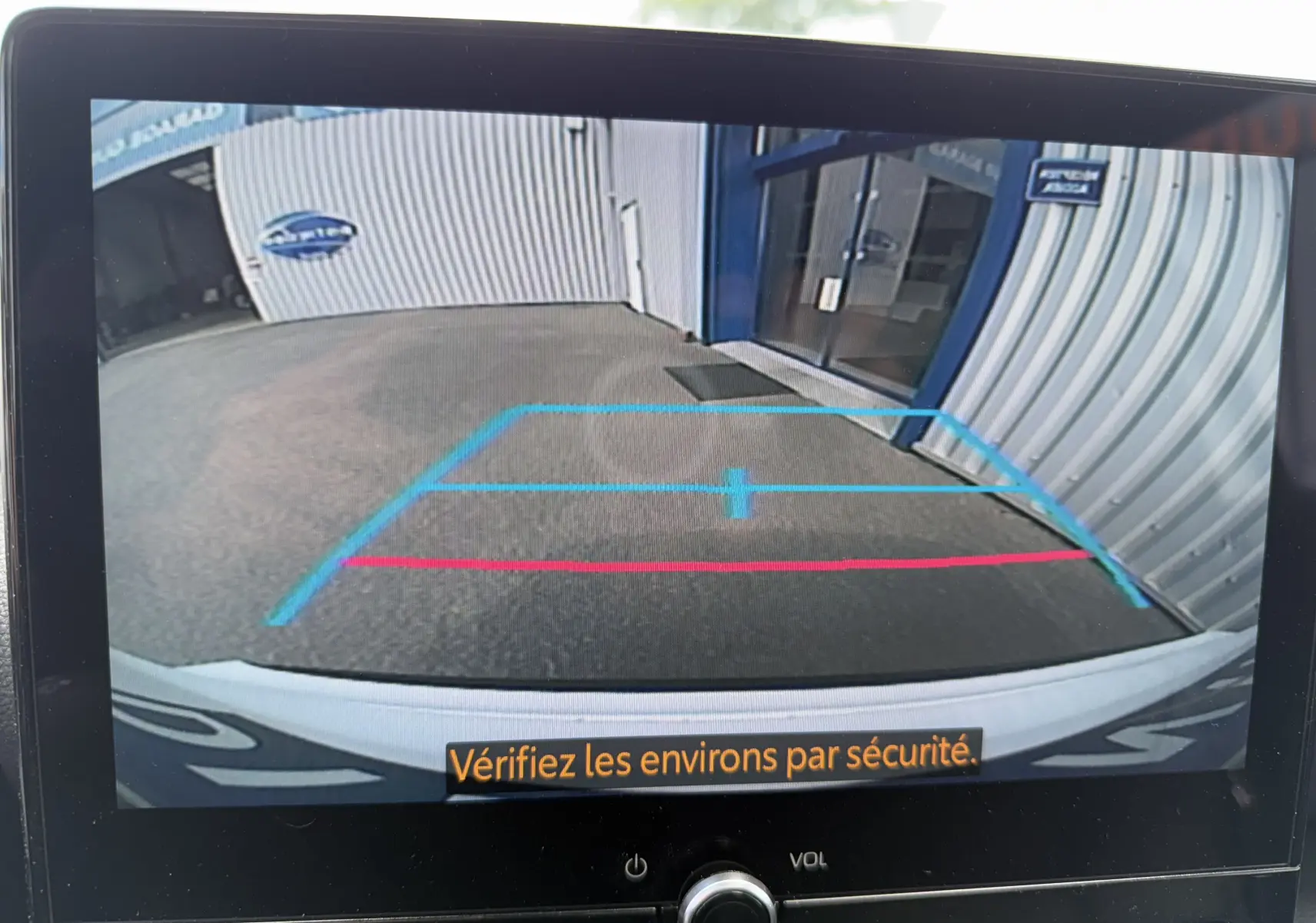 Vue arrière depuis la caméra de recul d'une Toyota Yaris Cross blanche 2024, avec lignes de guidage bleues et rouges visibles.