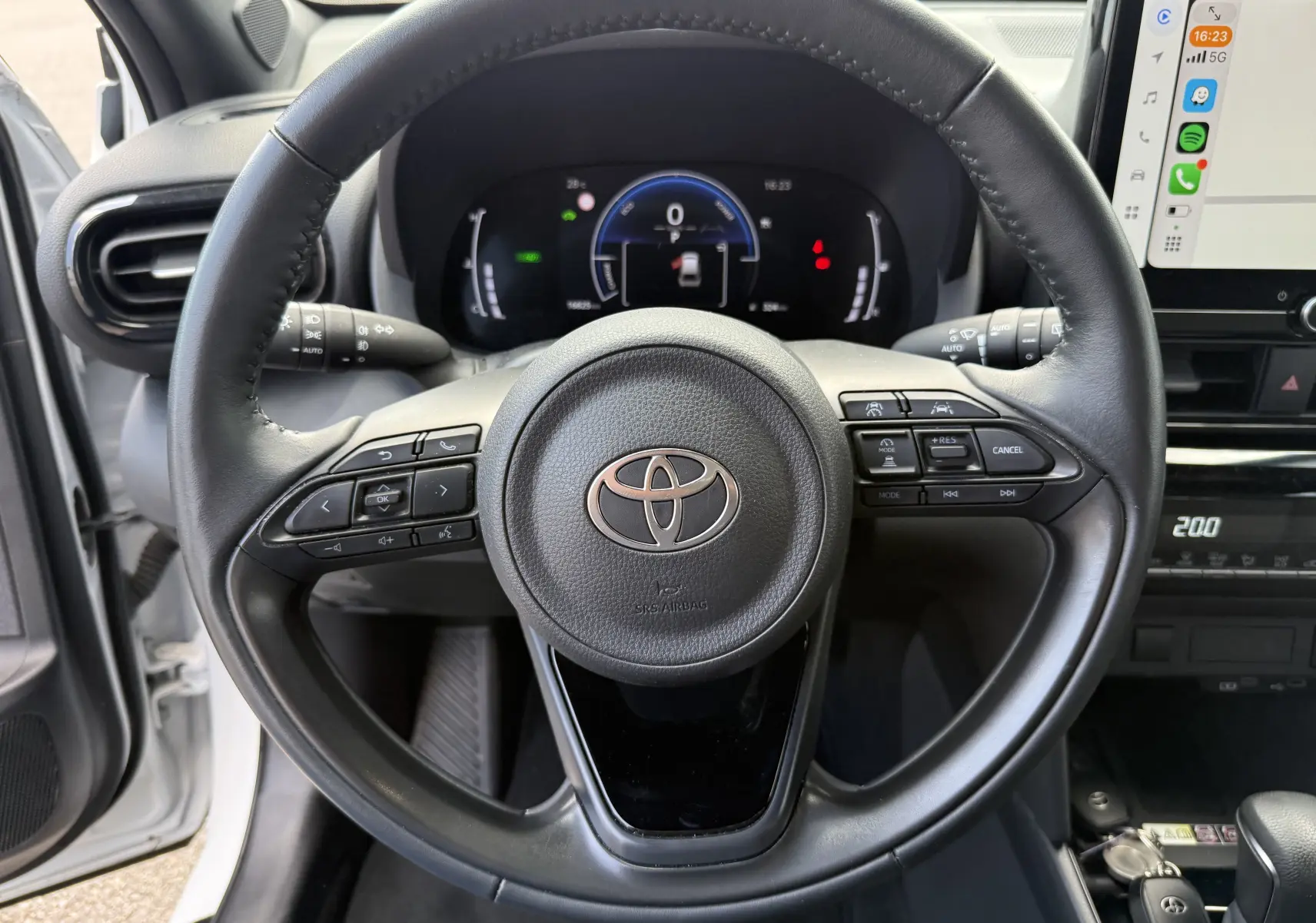 Vue intérieure centrée sur le volant noir de la Toyota Yaris Cross 130 CH Design 2024, avec tableau de bord digital et écran tactile visible.