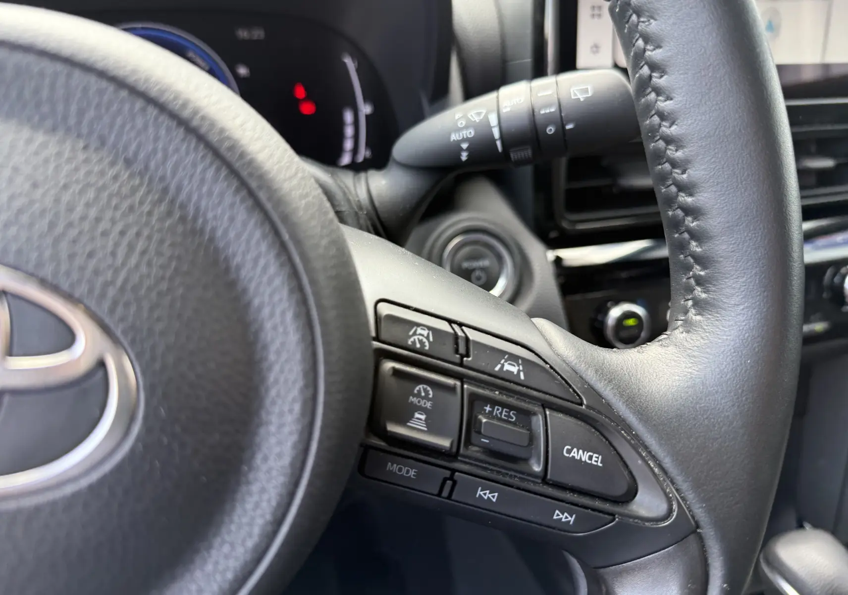 Gros plan sur le volant en cuir noir de la Toyota Yaris Cross 2024, avec commandes de régulateur de vitesse et aides à la conduite.