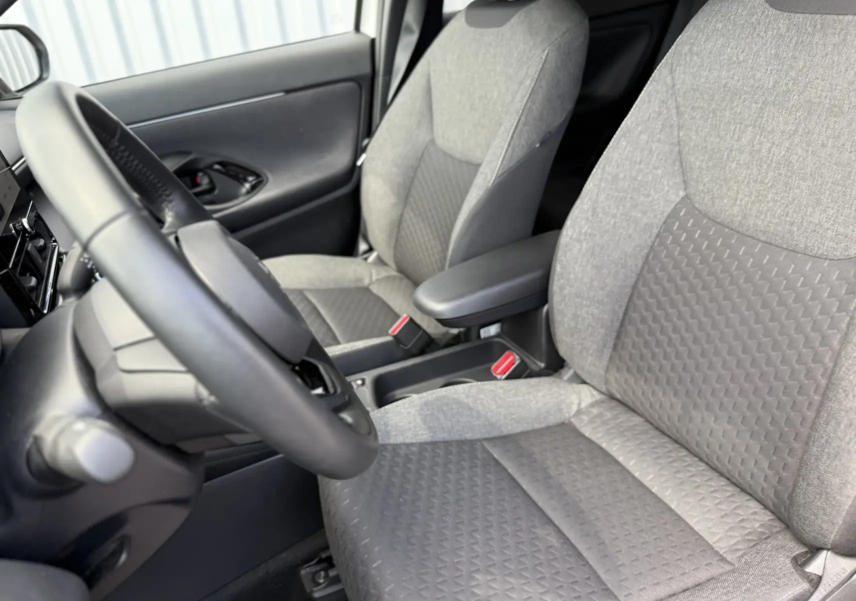 Vue intérieure côté conducteur de la Toyota Yaris Cross 130 CH Design 2024, sièges tissu gris avec accoudoir central.