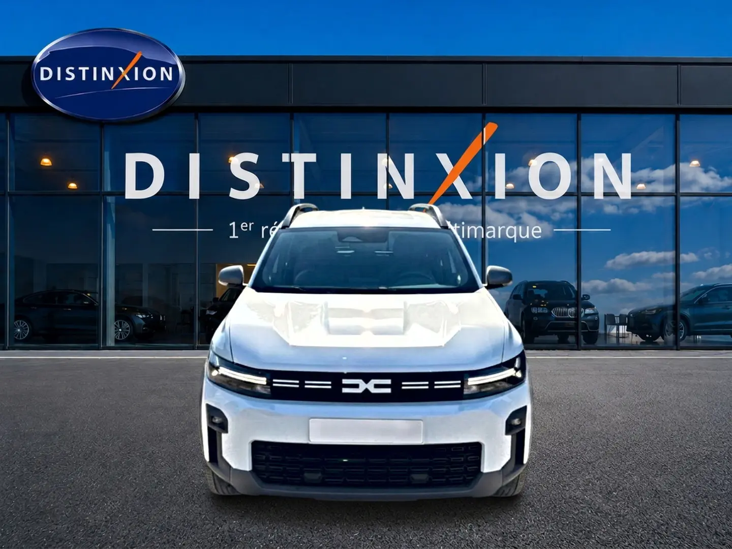 Vue avant d'un Dacia Bigster blanc 2026 avec calandre noire et barres de toit visibles devant une vitrine Distinxion.