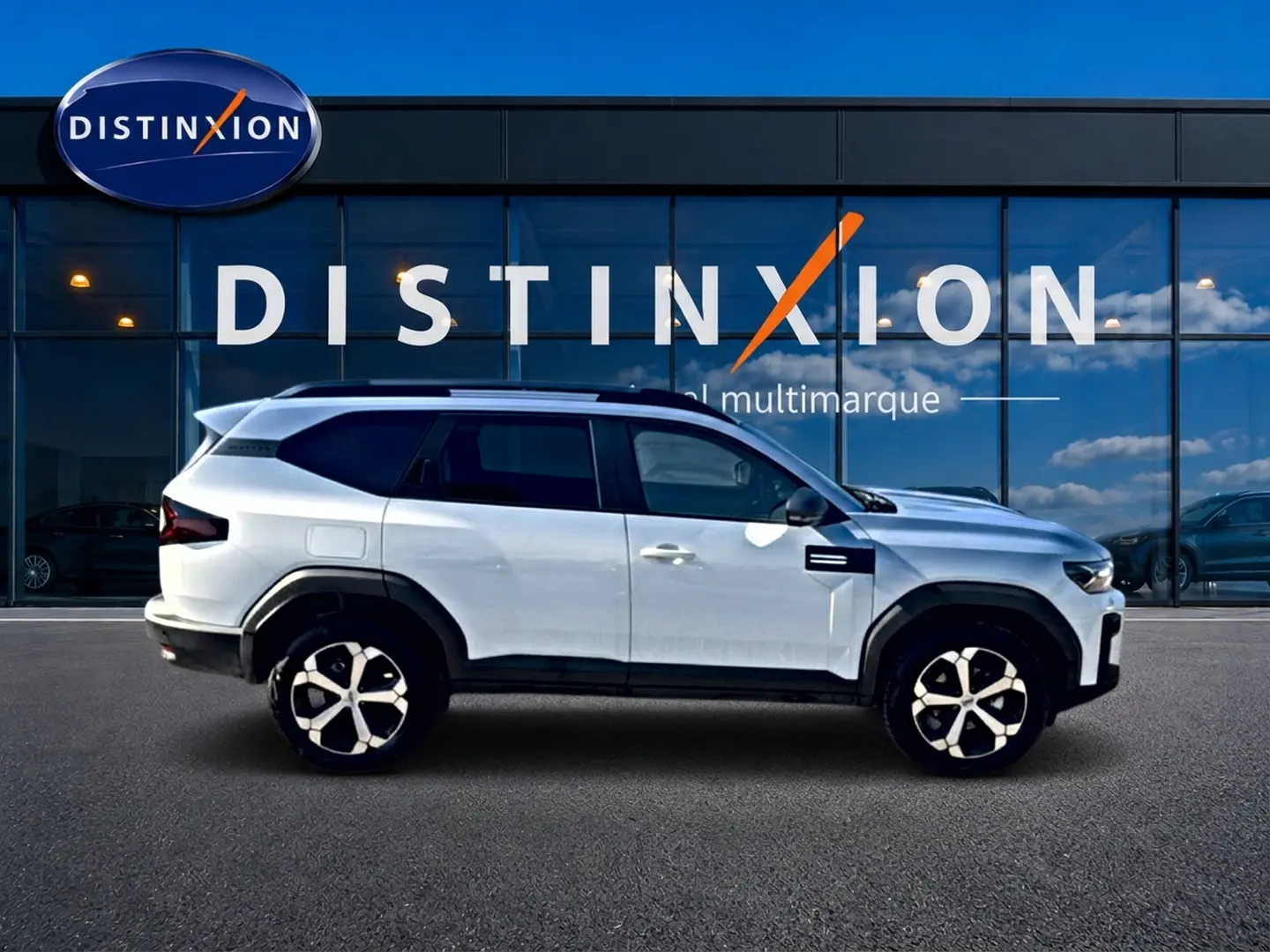 Profil droit du Dacia Bigster blanc 2026 avec jantes alu et barres de toit devant une vitrine Distinxion.