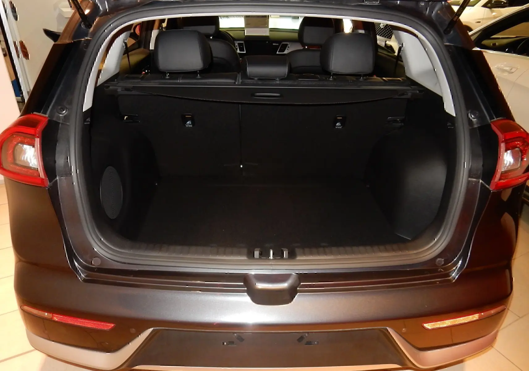 Coffre ouvert vu de l'arrière d'un KIA Niro hybride gris galène métal, montrant l'espace de chargement et les sièges arrière.