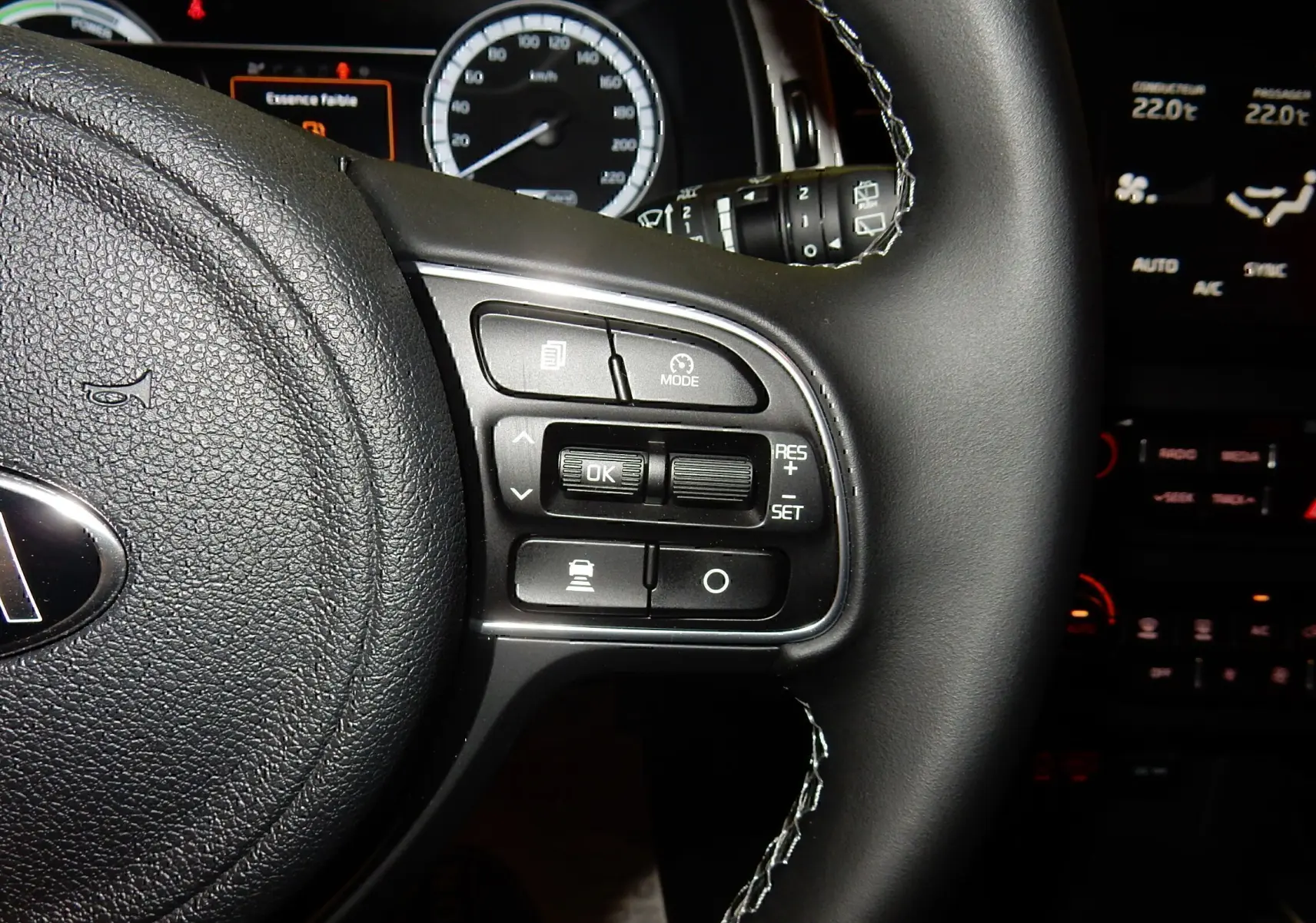 Gros plan sur le volant noir de la Kia Niro hybride 2019, montrant les commandes de régulateur et tableau de bord éclairé.