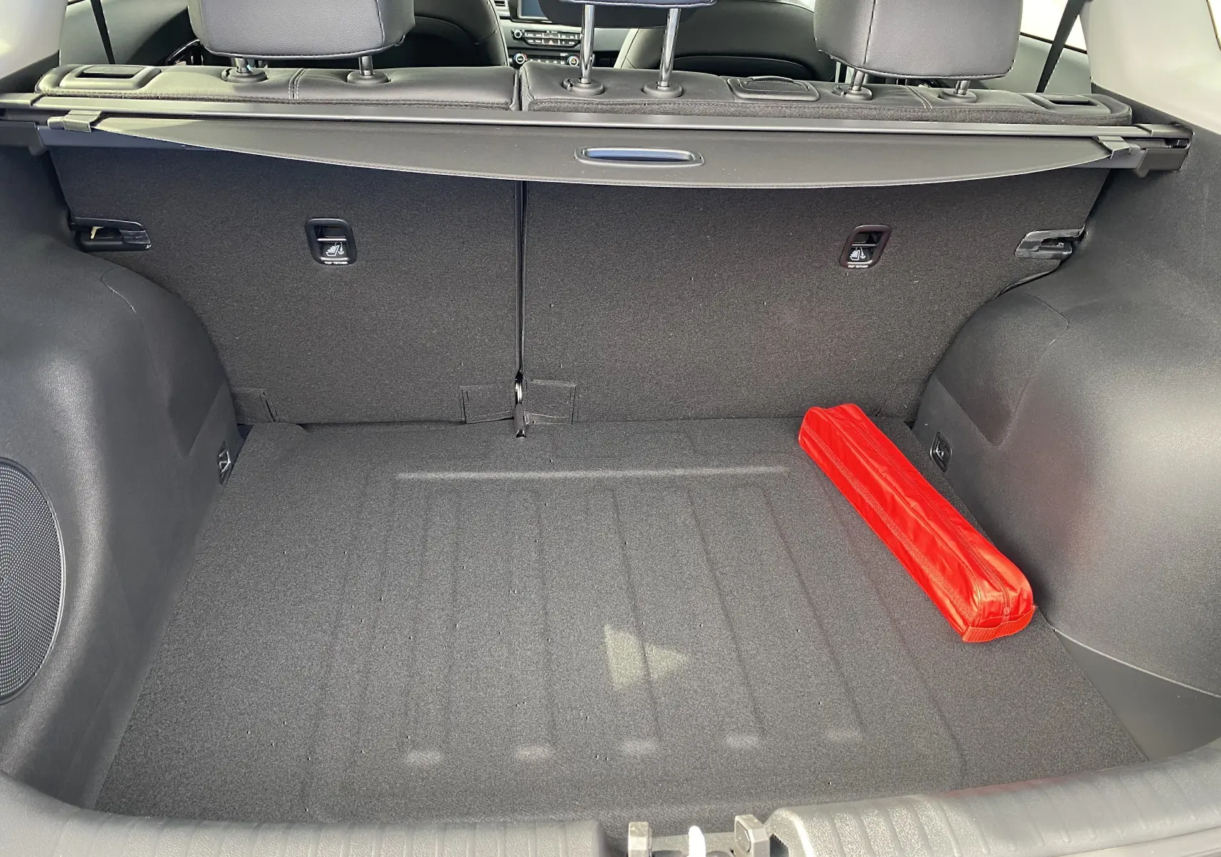 Coffre arrière vu de l'intérieur d'un Kia Niro gris galène, avec un triangle de signalisation rouge rangé à droite.
