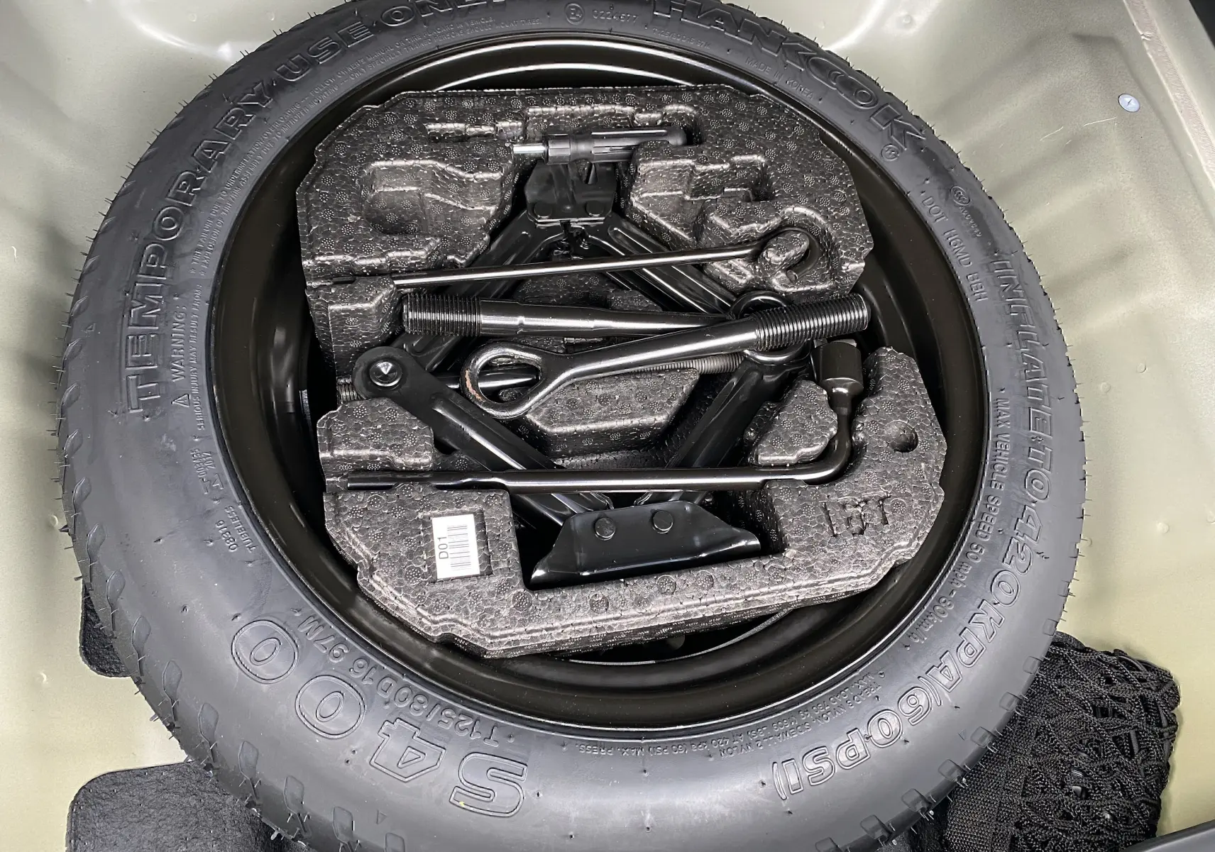 Roue de secours avec outils de changement rangés dans le coffre d’un KIA Niro hybride gris galène 2019.