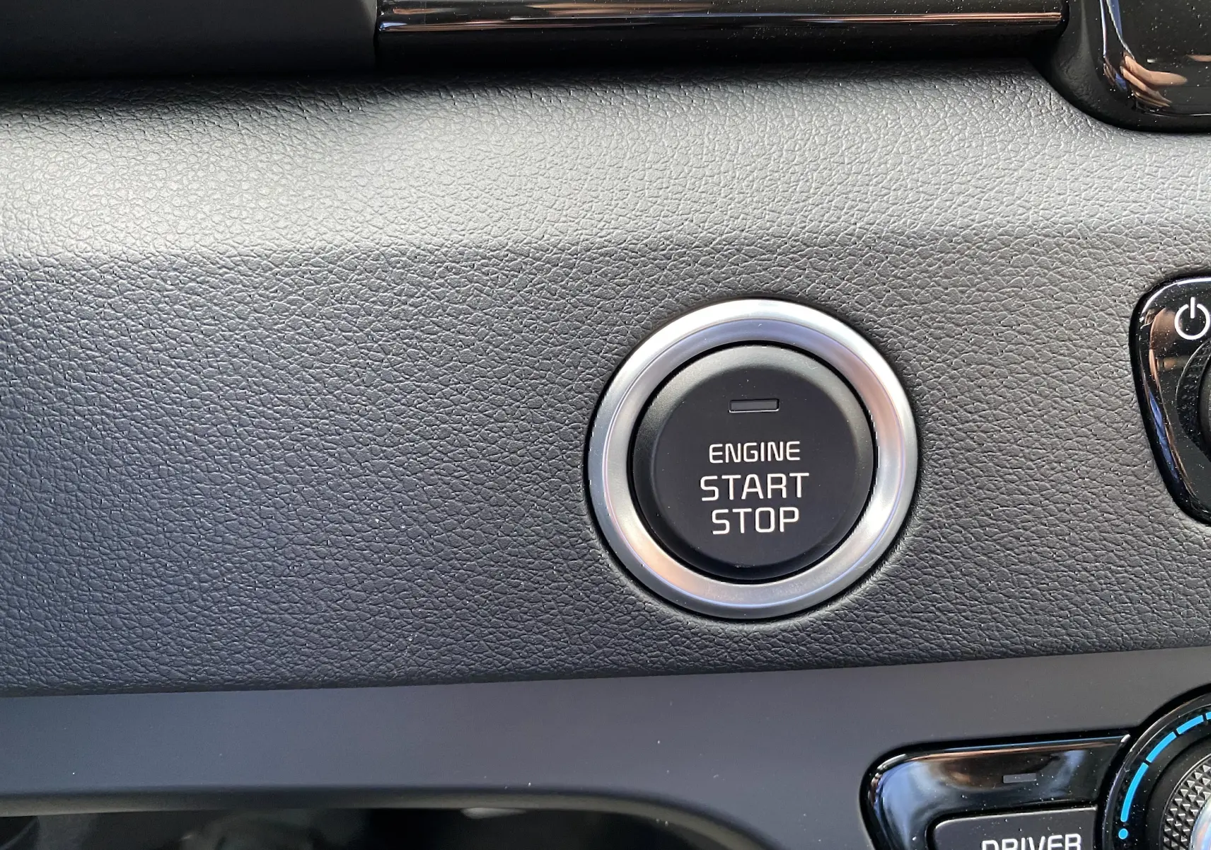 Gros plan sur le bouton start/stop du moteur dans l’habitacle du Kia Niro hybride gris galène, tableau de bord texturé noir.