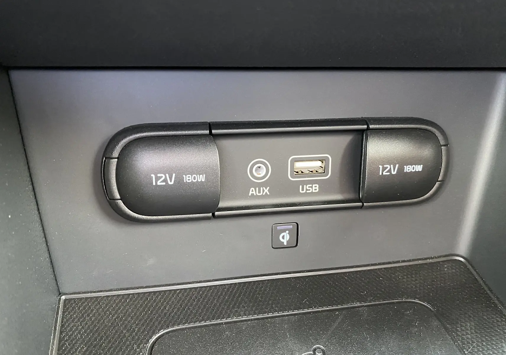 Gros plan sur la console centrale du Kia Niro hybride 2019, montrant prises 12V, port AUX et USB, avec surface de recharge sans fil.