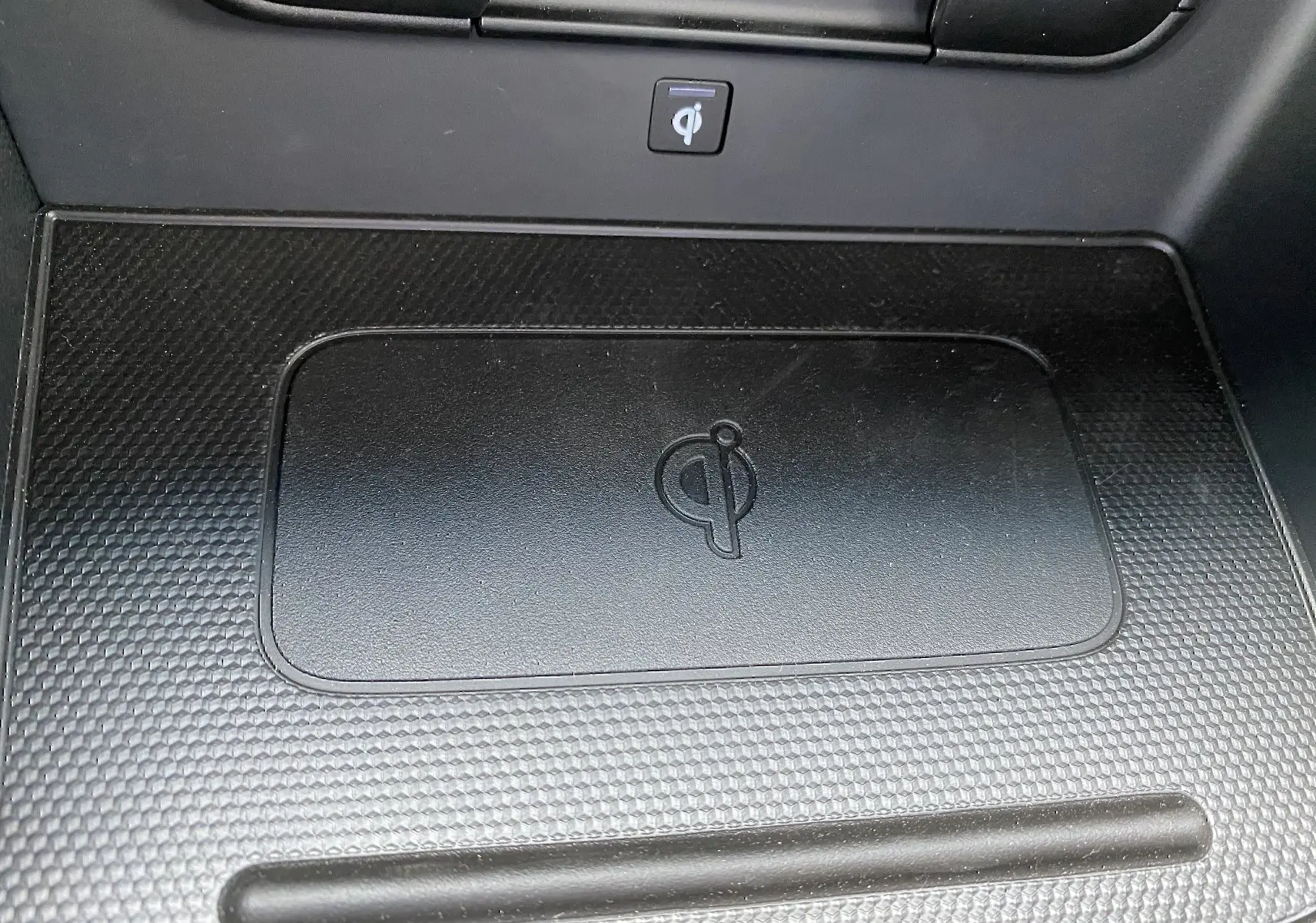 Détail du chargeur à induction noir avec logo Qi dans l'habitacle du Kia Niro hybride gris galène 2019.