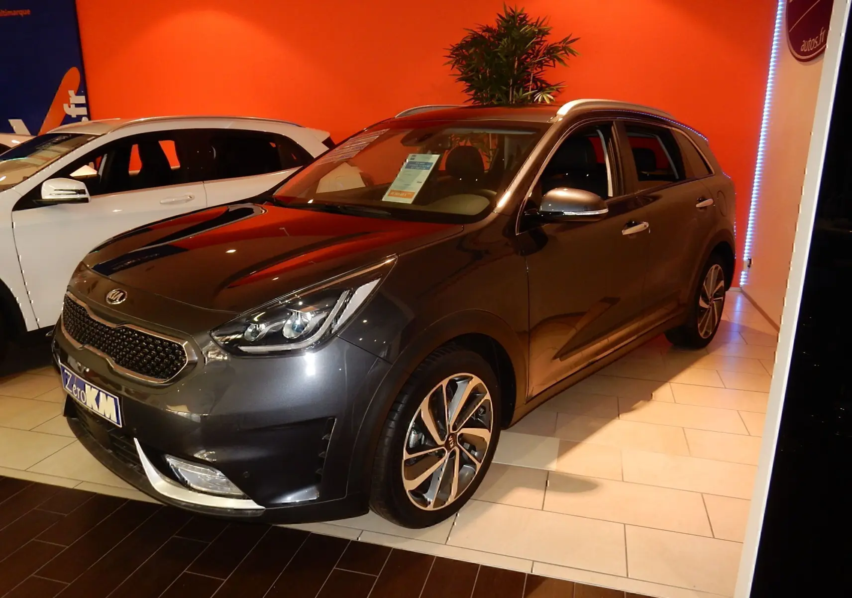 KIA Niro hybride gris galène métal en 3/4 avant droit, avec jantes alliage et calandre distinctive en showroom.