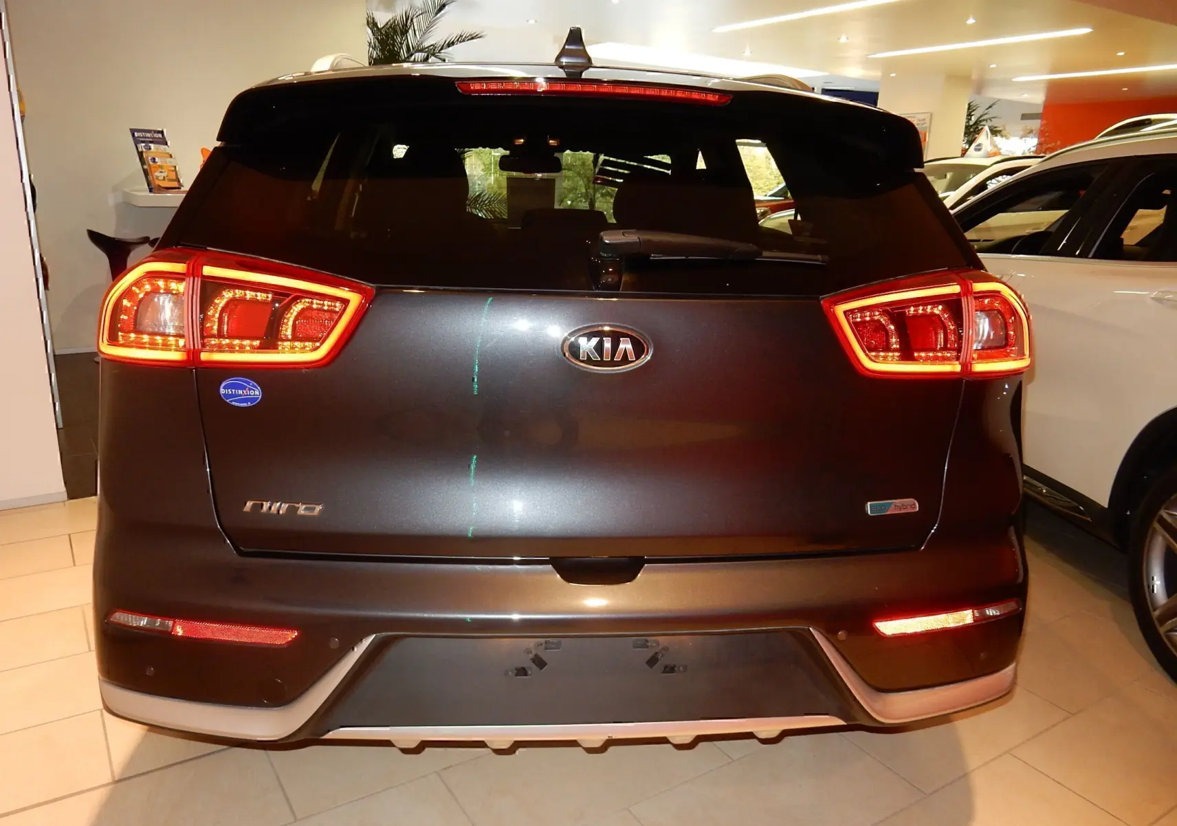 Vue arrière d'un KIA Niro hybride gris galène métal avec feux arrière allumés en intérieur showroom.