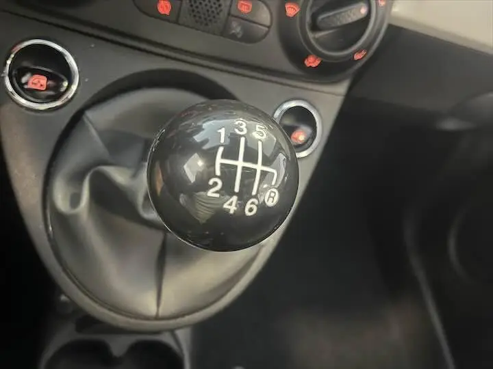 Le levier de vitesses manuel noir de la FIAT 500 blanche, vue rapprochée de la console centrale intérieure.