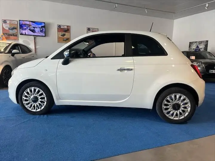 Profil droit d'une FIAT 500 blanche 2023 avec jantes alliage et poignée de porte chromée en showroom.