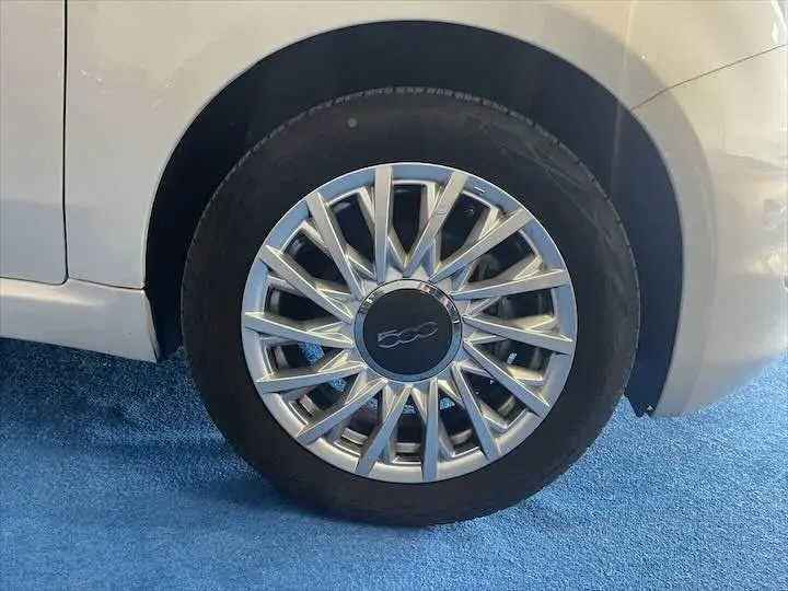 Gros plan sur la roue avant droite blanche d'une Fiat 500 2023 avec jante argentée au design étoilé.