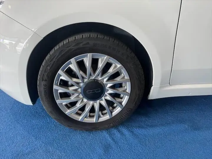 Gros plan sur la roue arrière droite d'une FIAT 500 blanche 2023, avec jante argentée au design étoilé.