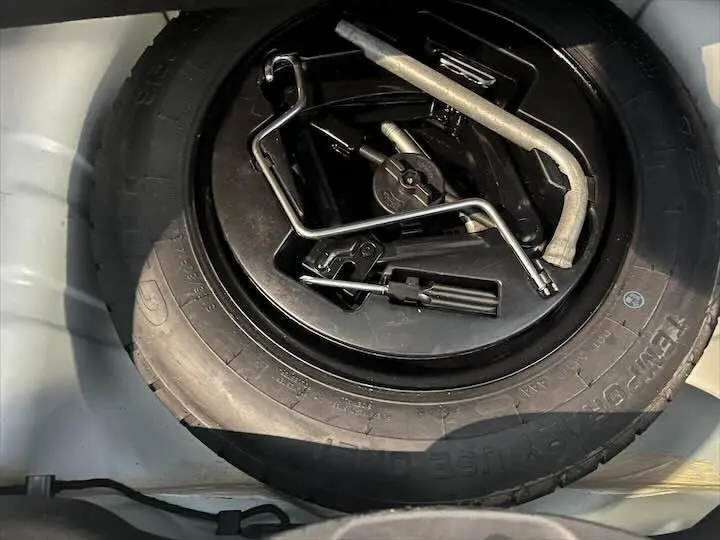 Gros plan sur la roue de secours et les outils de bord dans le coffre d'une FIAT 500 blanche 2023.