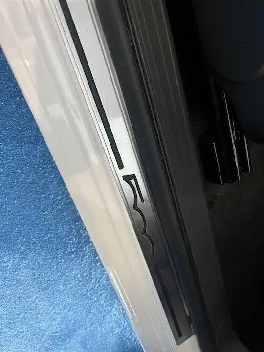 Gros plan sur la plaque de seuil de porte côté gauche blanche d'une Fiat 500 avec logo 500 noir.