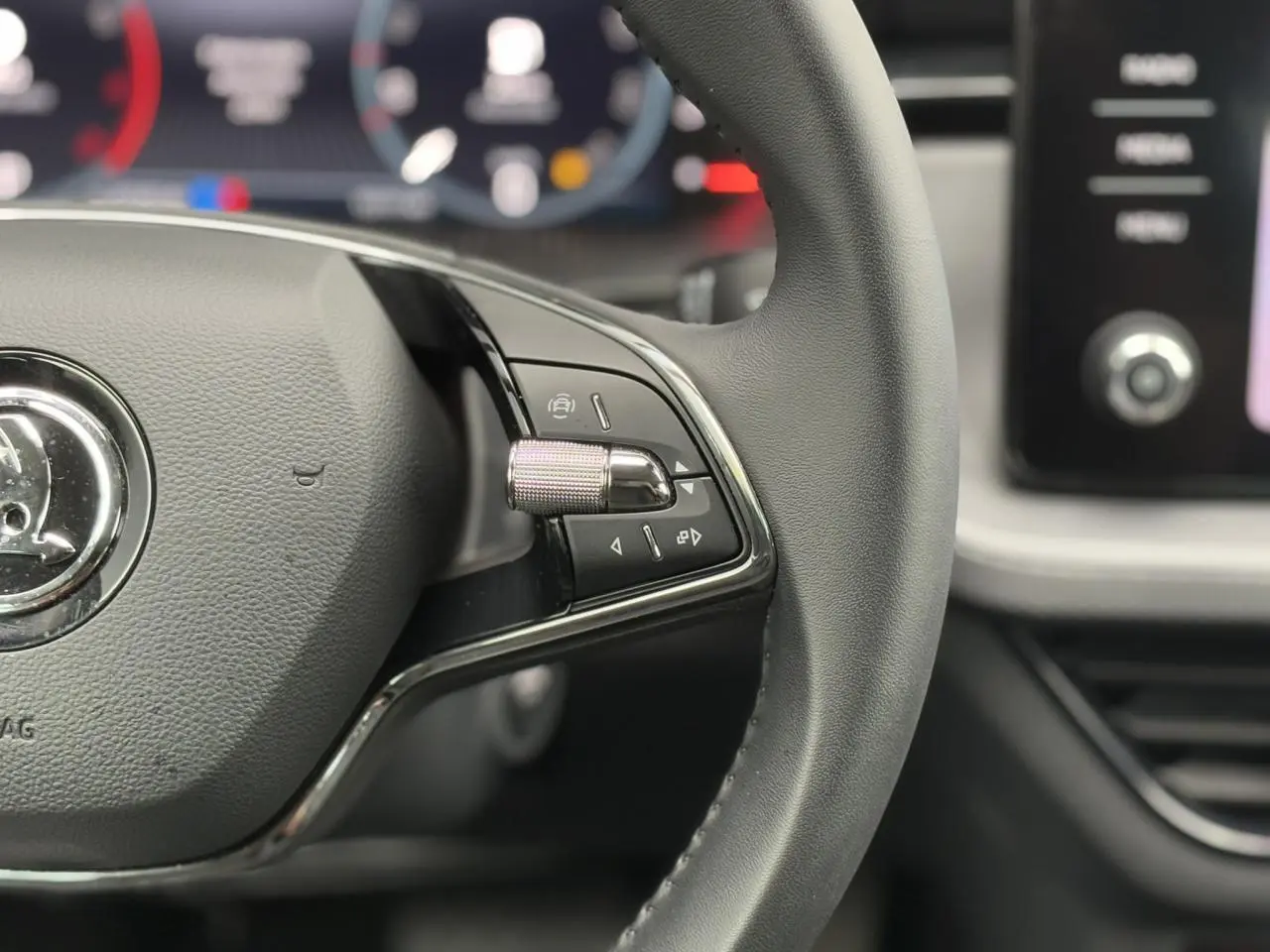 Gros plan sur le volant cuir noir de la Skoda Scala 2024 avec commandes multifonctions côté droit et tableau de bord numérique flou.