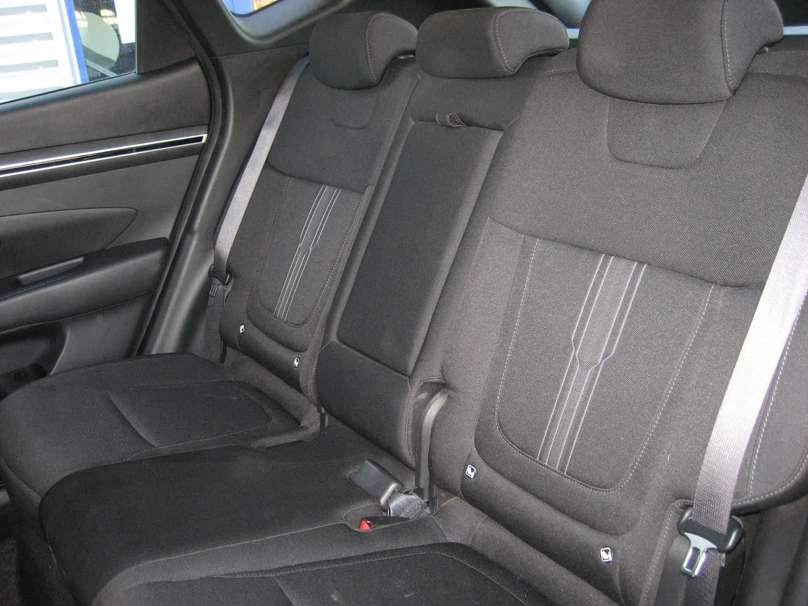 Vue intérieure des sièges arrière noirs du Hyundai Tucson III 2022, avec appuie-têtes et ceintures visibles côté gauche.