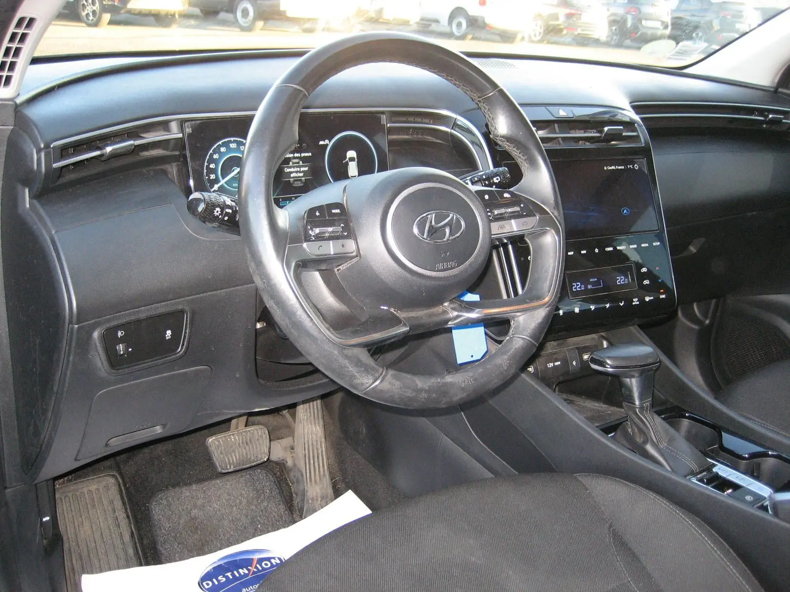 Vue intérieure du tableau de bord et volant noir du Hyundai Tucson III hybride, avec écran tactile et levier de vitesse automatique.
