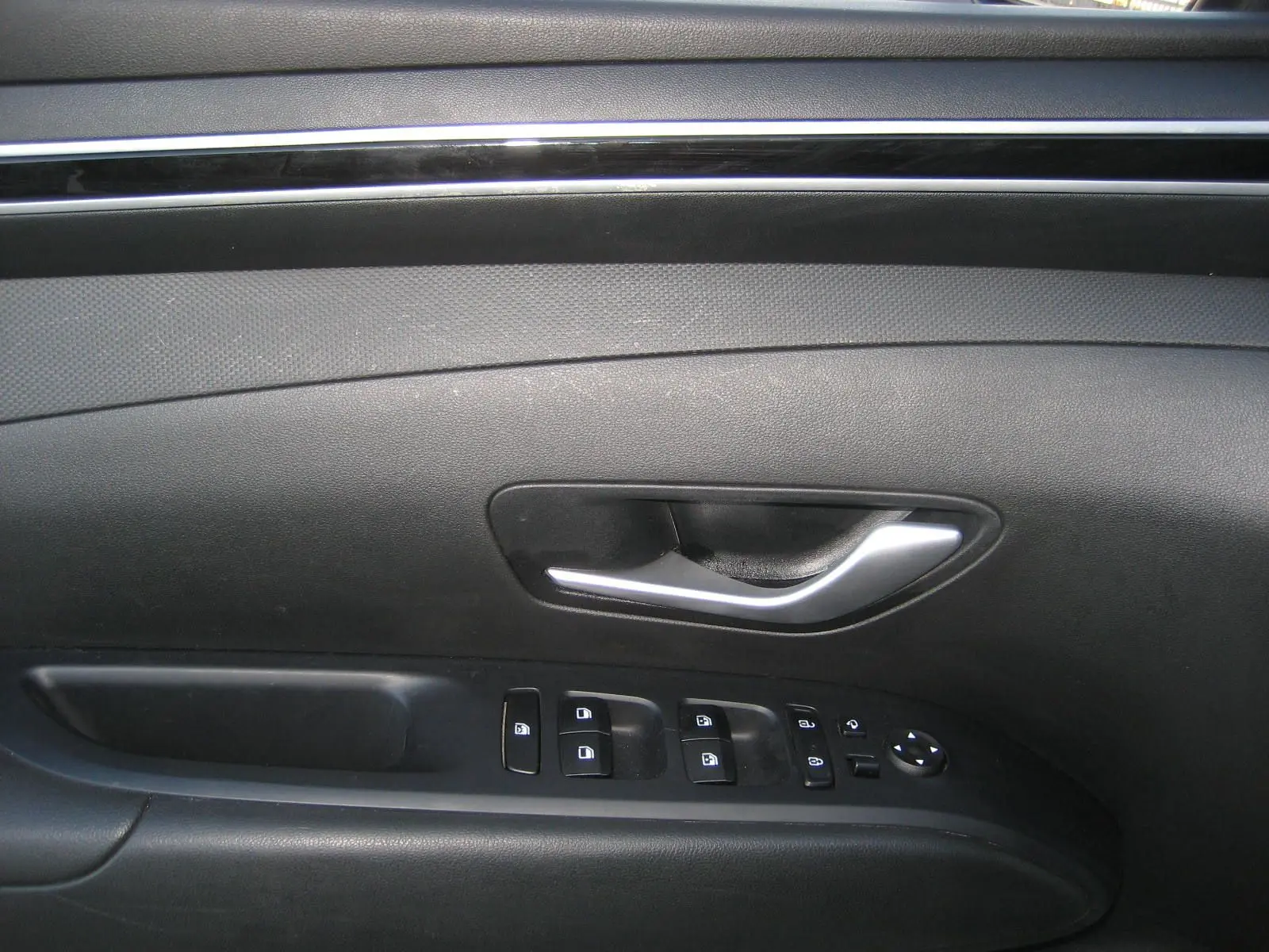 Poignée de porte intérieure côté gauche noire du Hyundai Tucson III 2022 avec commandes électriques des vitres et rétroviseurs.