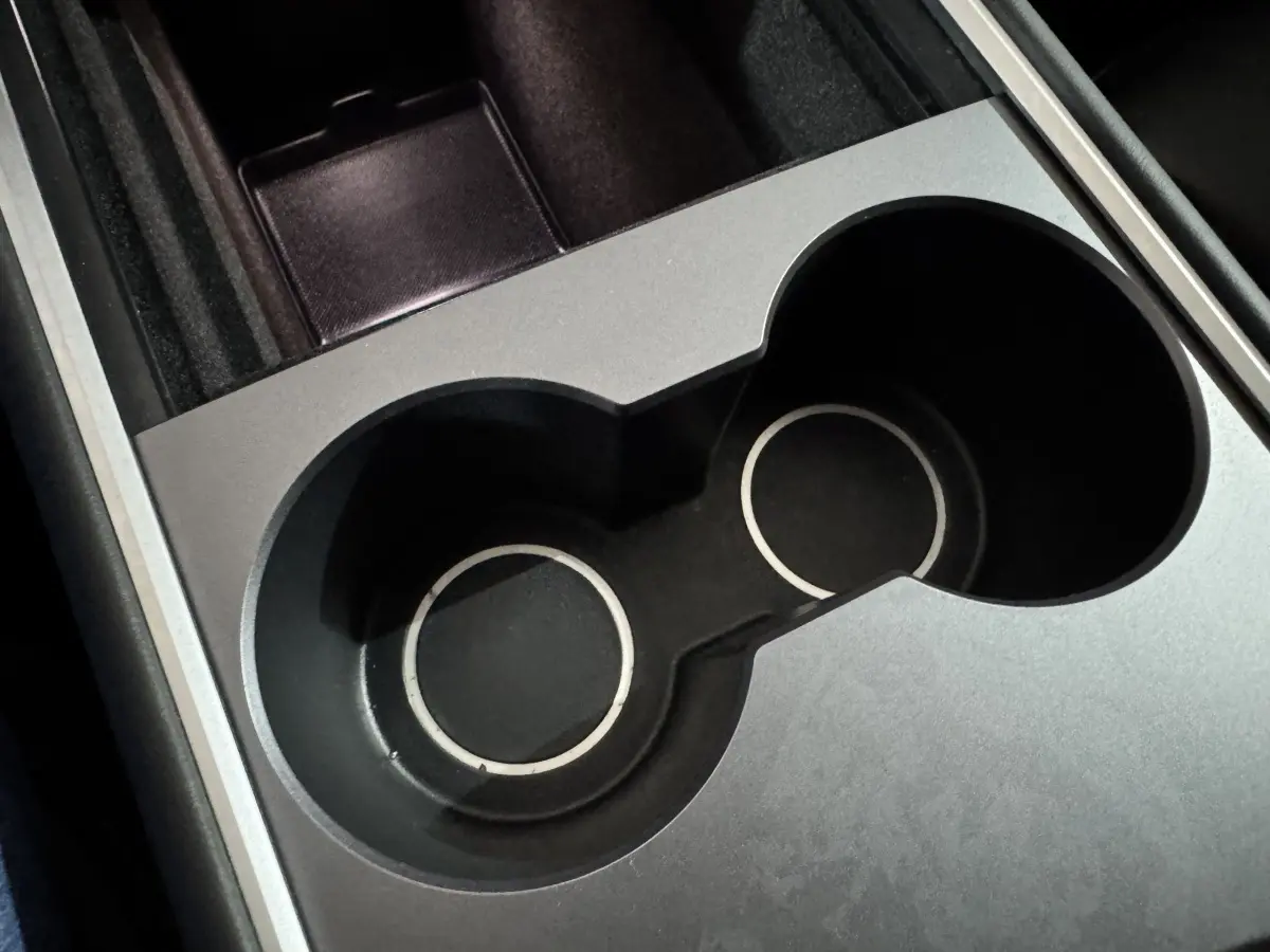 Gros plan sur les porte-gobelets noirs et argentés de la console centrale d'une Tesla Model Y blanche électrique.