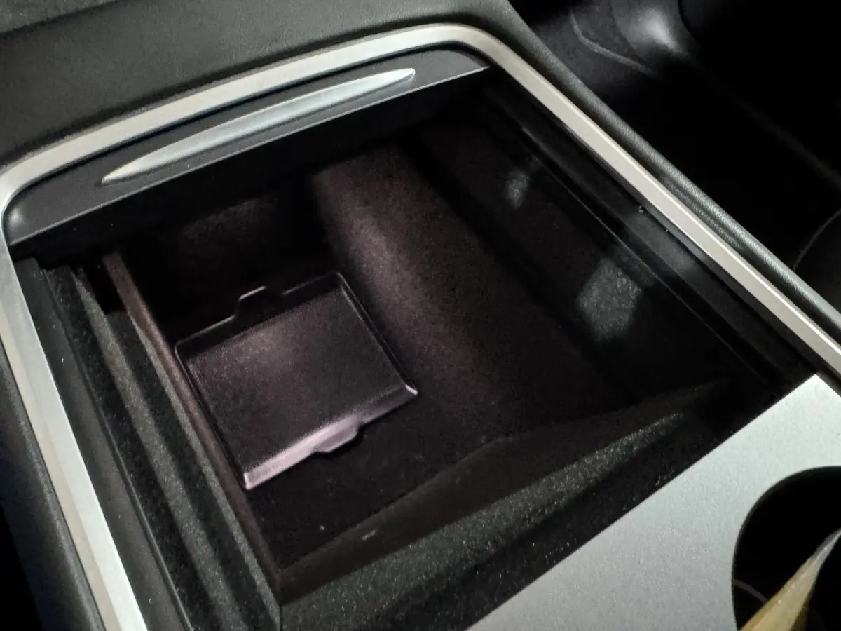 Vue rapprochée de la console centrale noire et argentée du Tesla Model Y blanc, mettant en valeur le rangement intérieur.